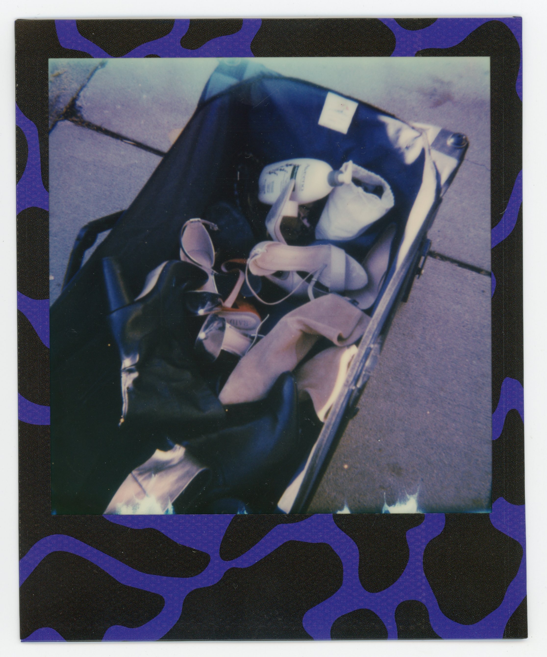 Open suitcase on pavement containing various personal items, including a purse, toiletries, and clothes.