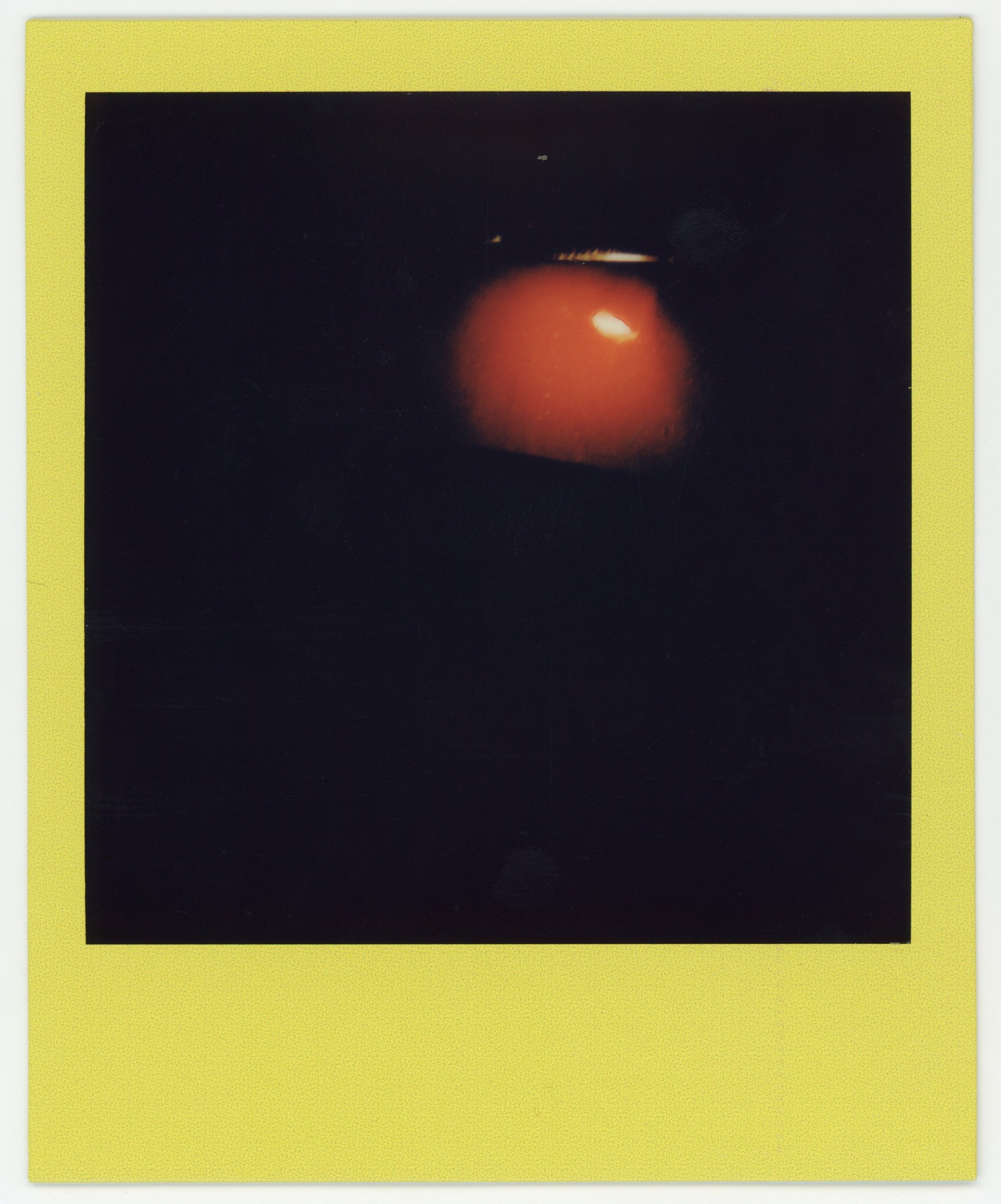 A dark photograph with a glowing, reddish-orange orb near the center, with a few small bright spots above it.