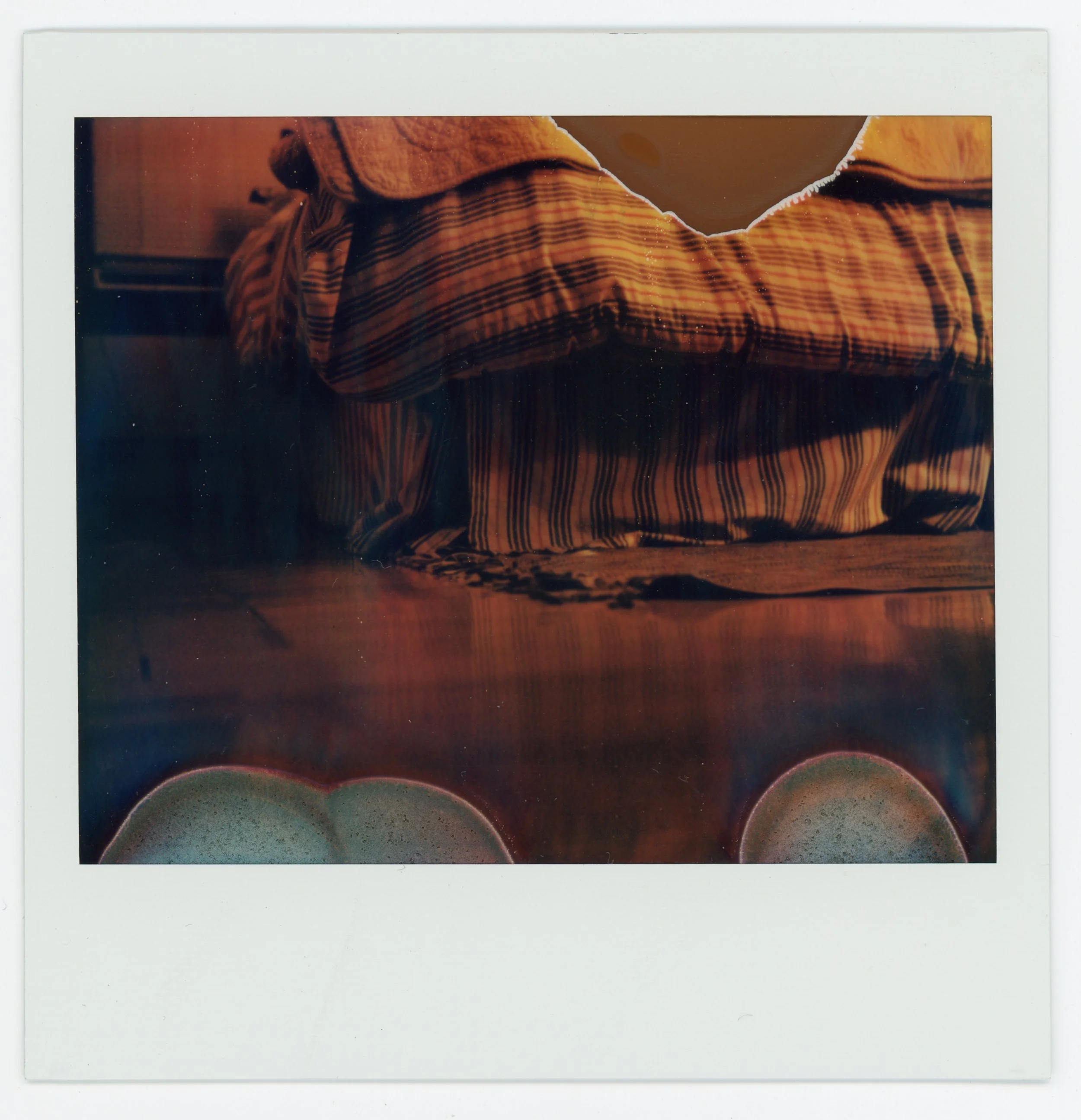 A Polaroid photo of a person wearing a striped, patterned shirt sitting at a wooden table.