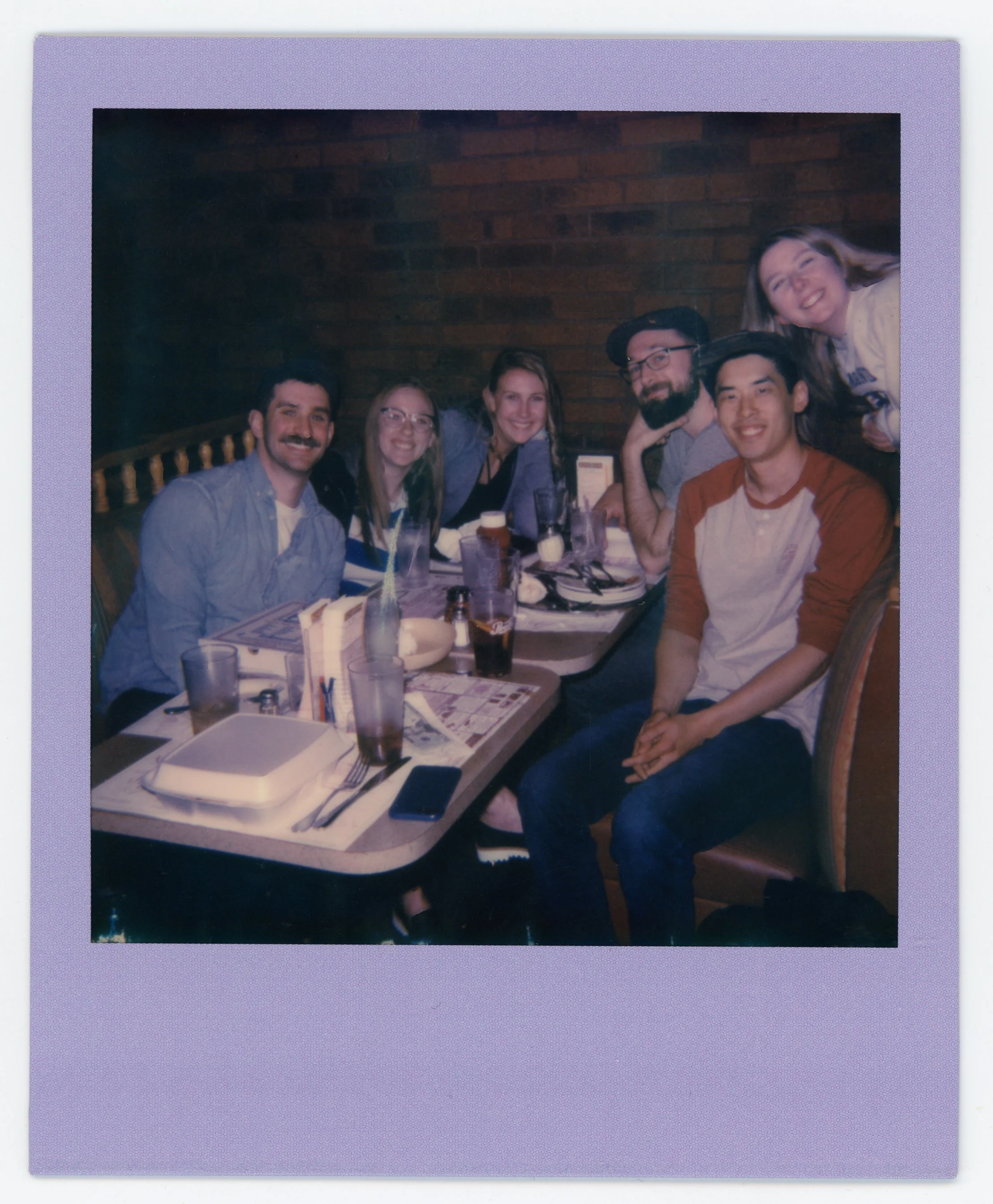 Group of seven friends smiling and sitting at a restaurant table with drinks and menus