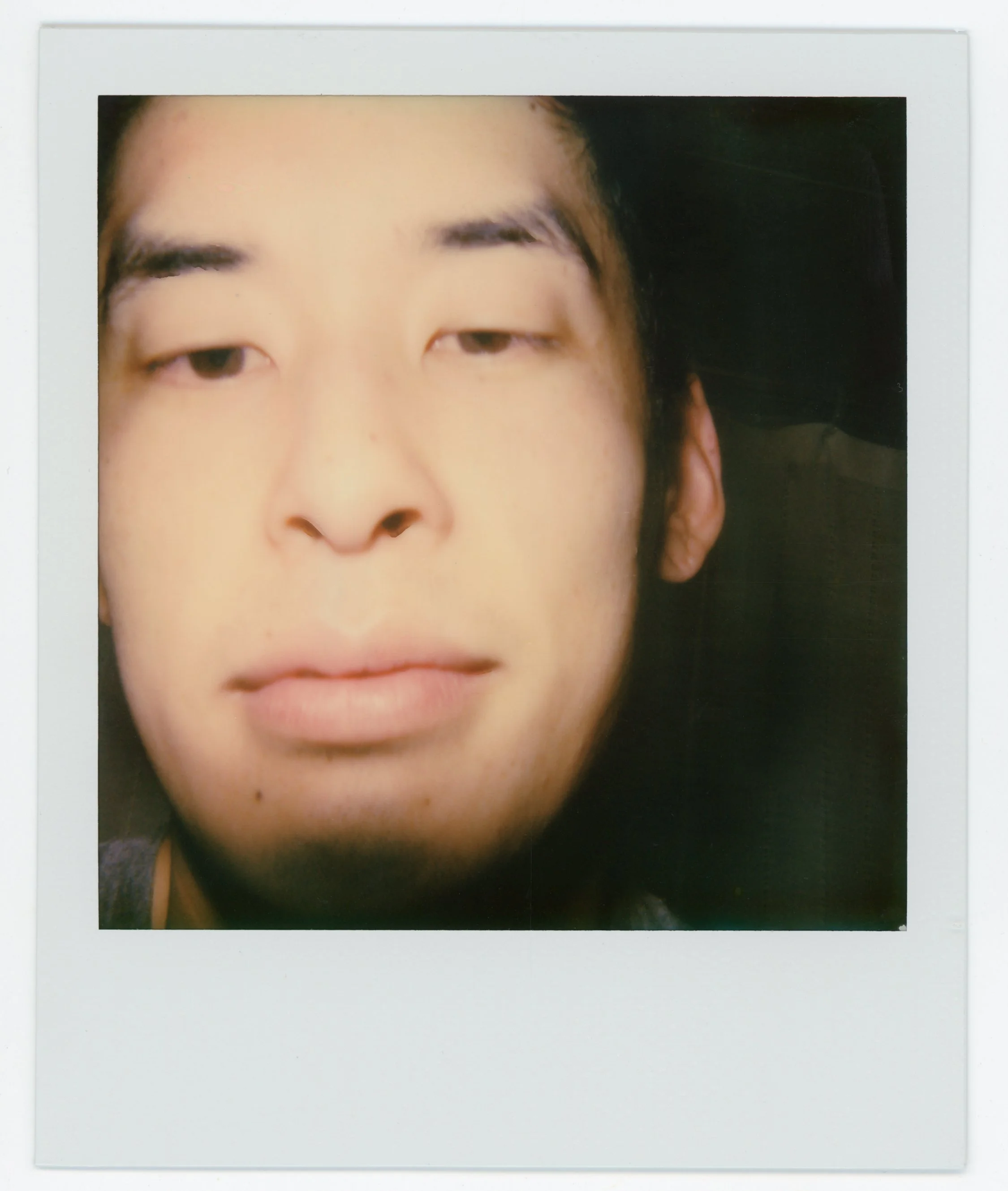 Close-up photo of a young Asian man's face with a relaxed expression, slightly squinting eyes, and dark background.