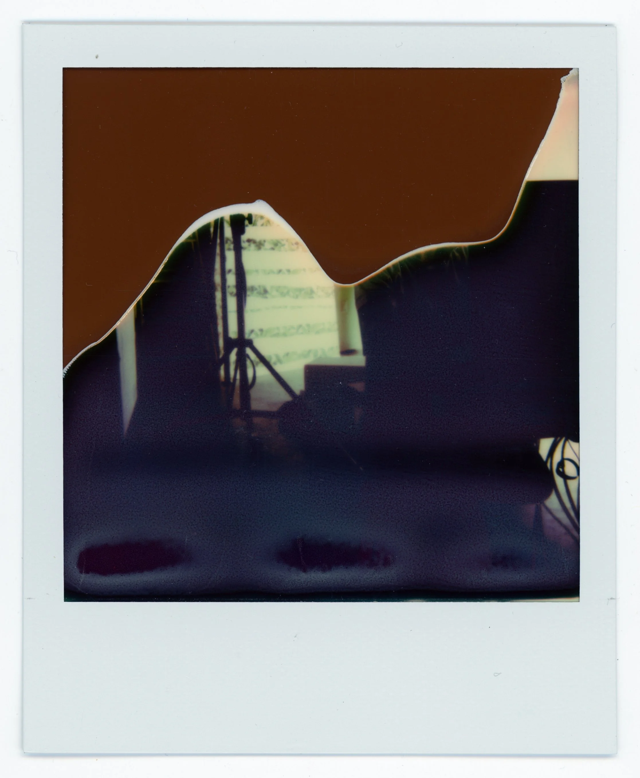 A Polaroid photo showing a torn or burned slide, with a silhouette of studio equipment and a window in the background.