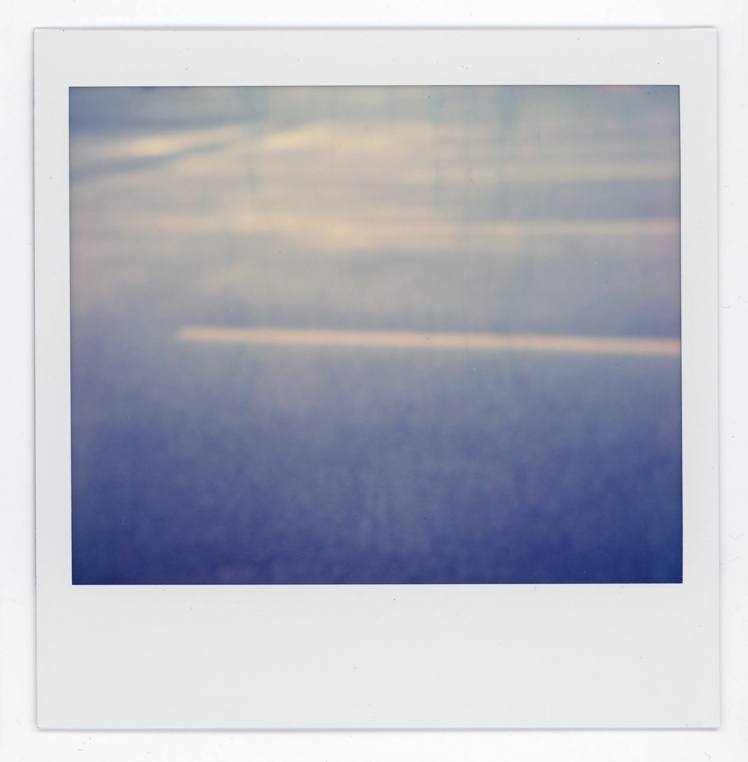 Polaroid photo of a cloudy sky over the ocean with a horizon in the distance.