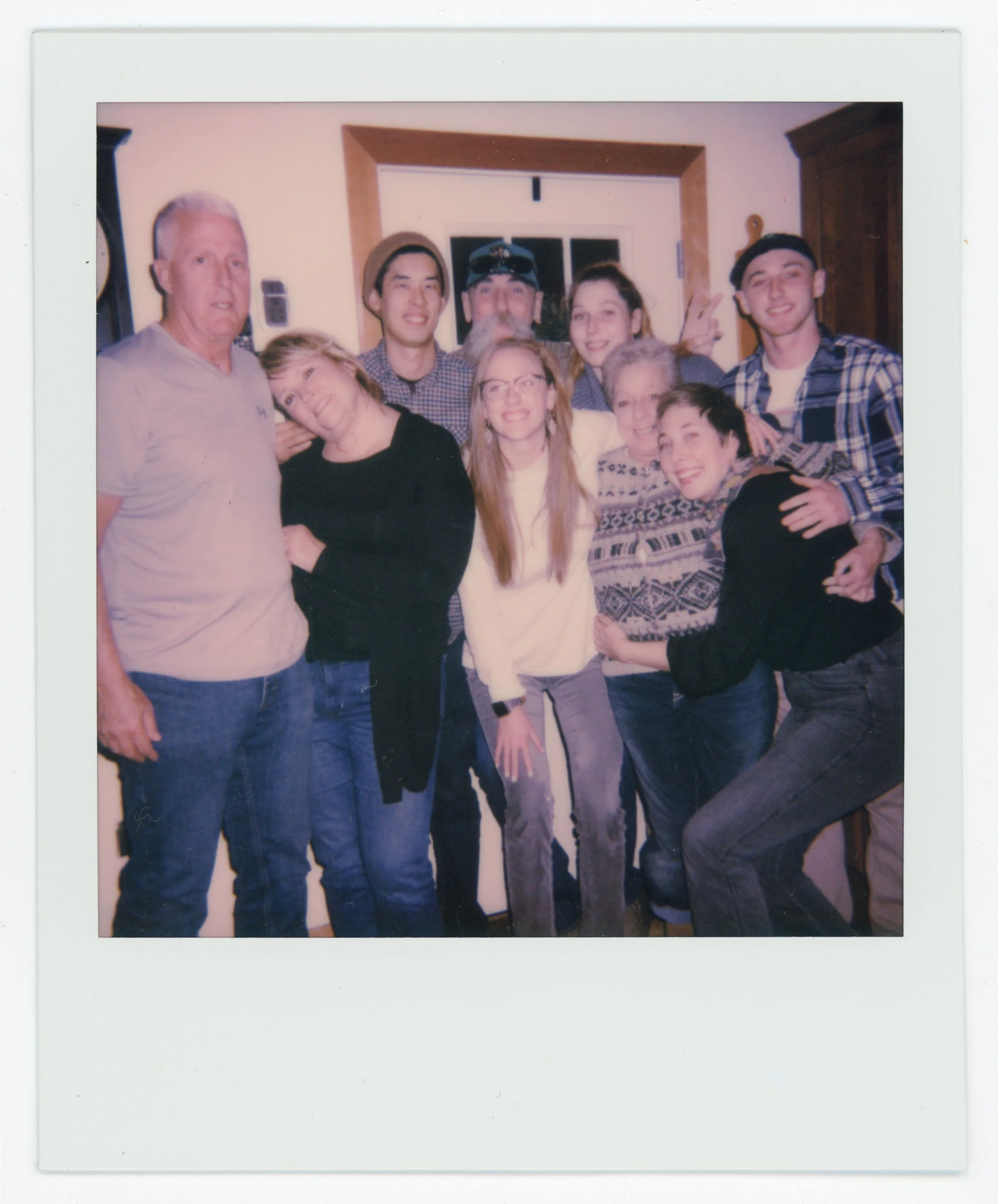 Group of nine people smiling and posing together indoors, some making peace signs.