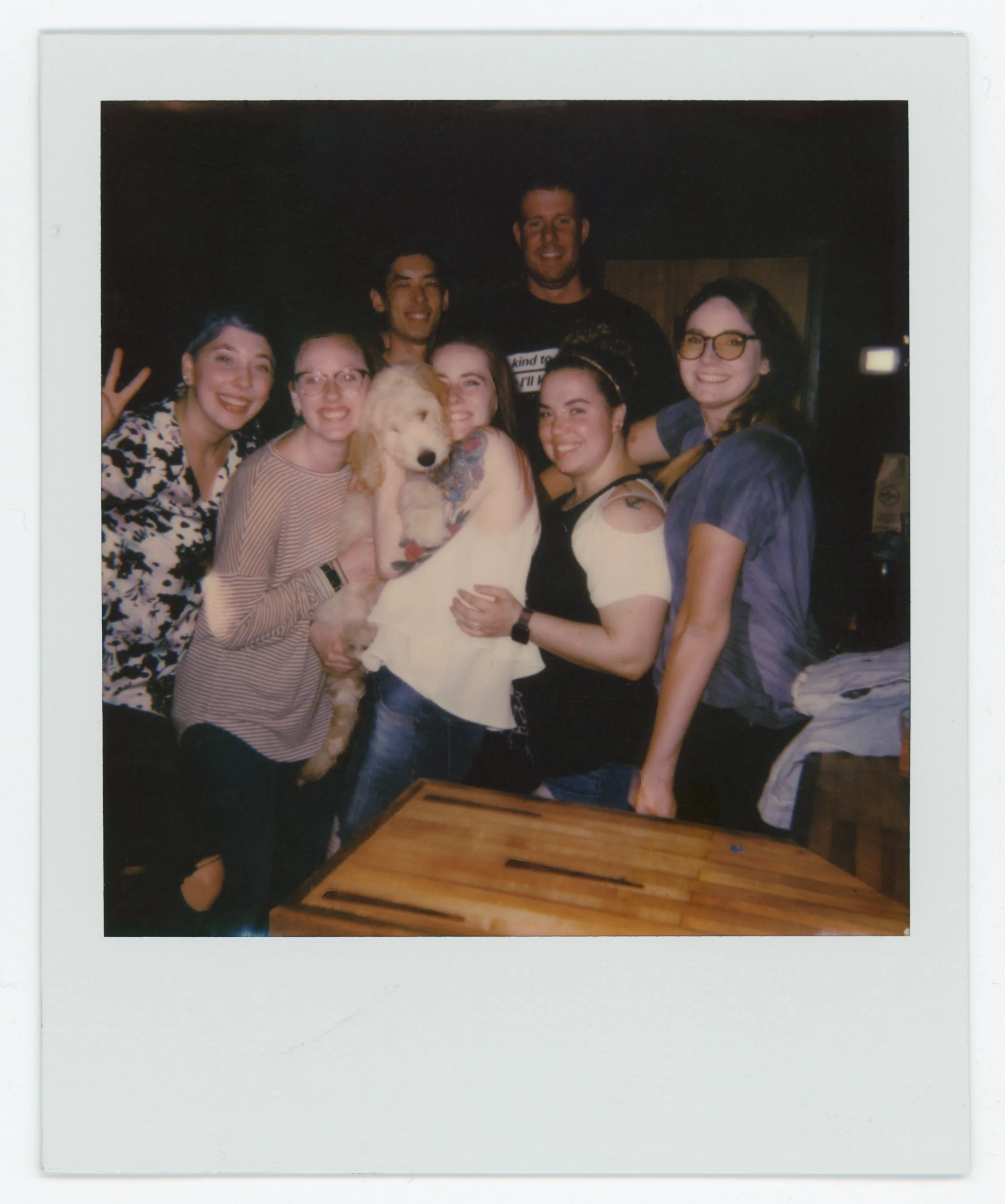 Group of people hugging and smiling with a dog in center at a social gathering.