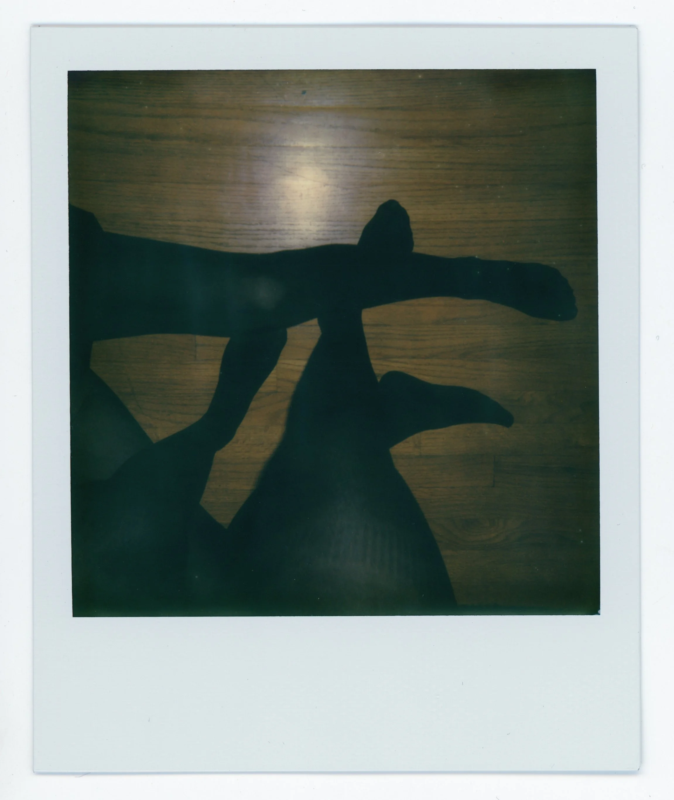 Silhouette of a person's legs crossed, seen from above, on a wooden floor.
