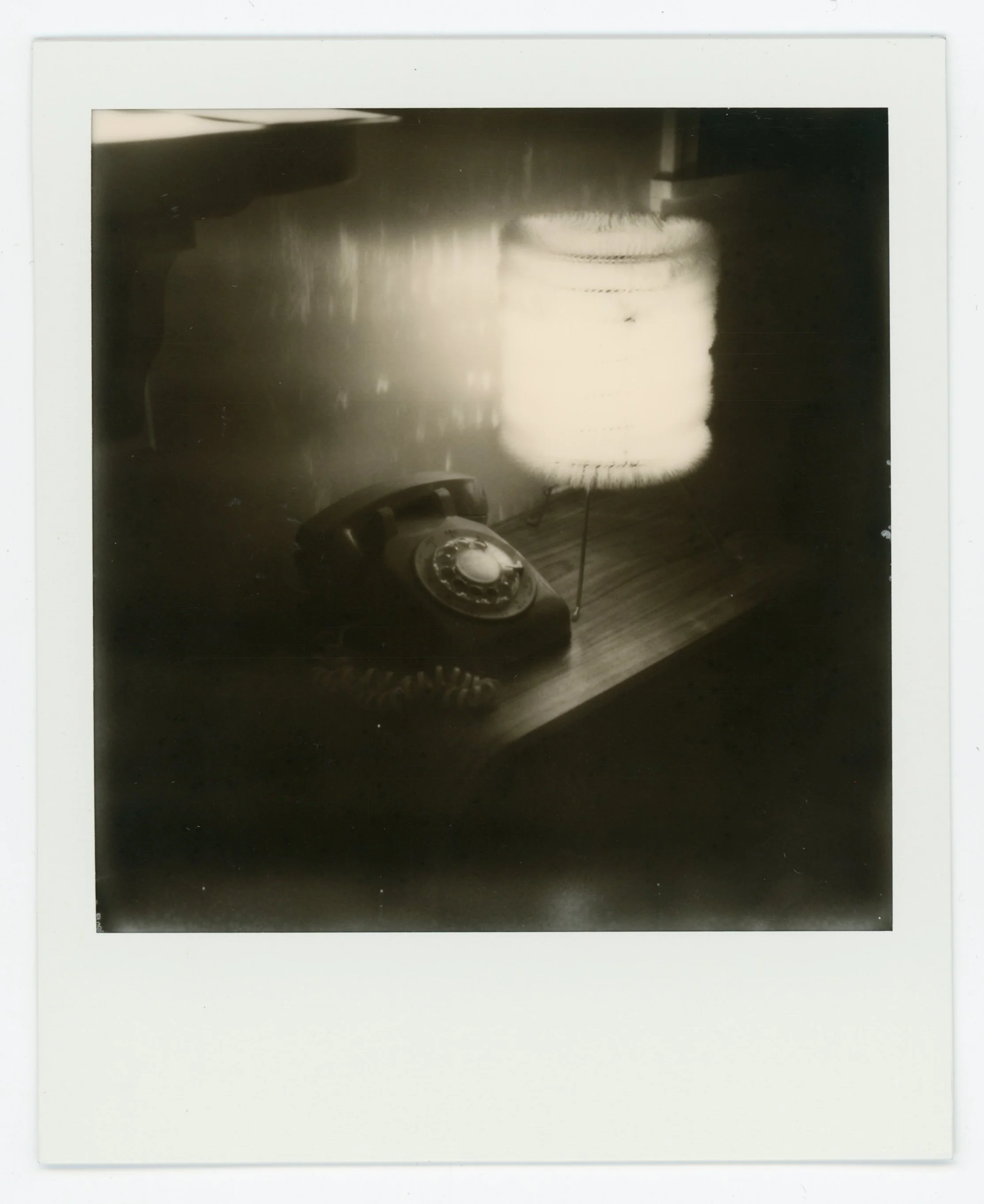 Black and white photograph of a vintage rotary telephone and a table lamp on a wooden surface.