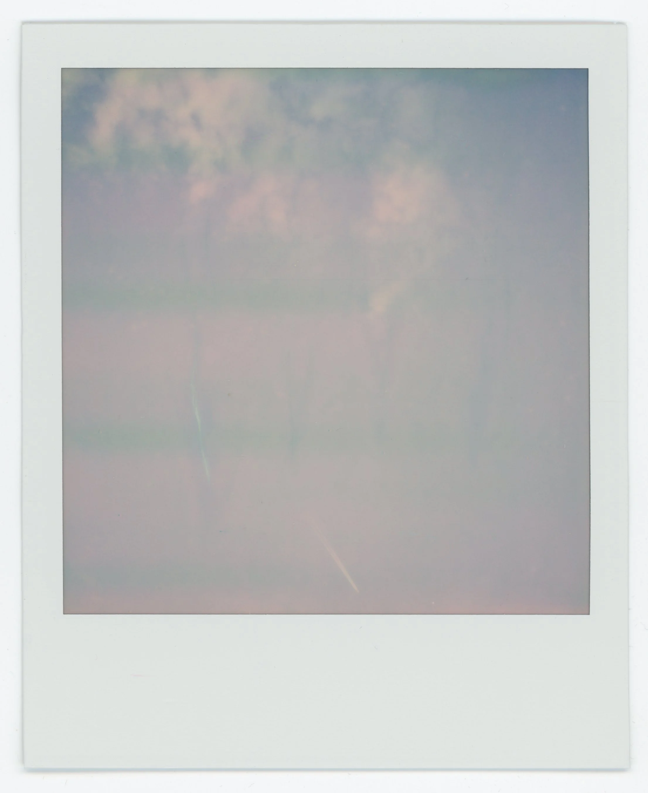 Polaroid photo of a sky with soft clouds and sunlight creating a pastel-colored scene.