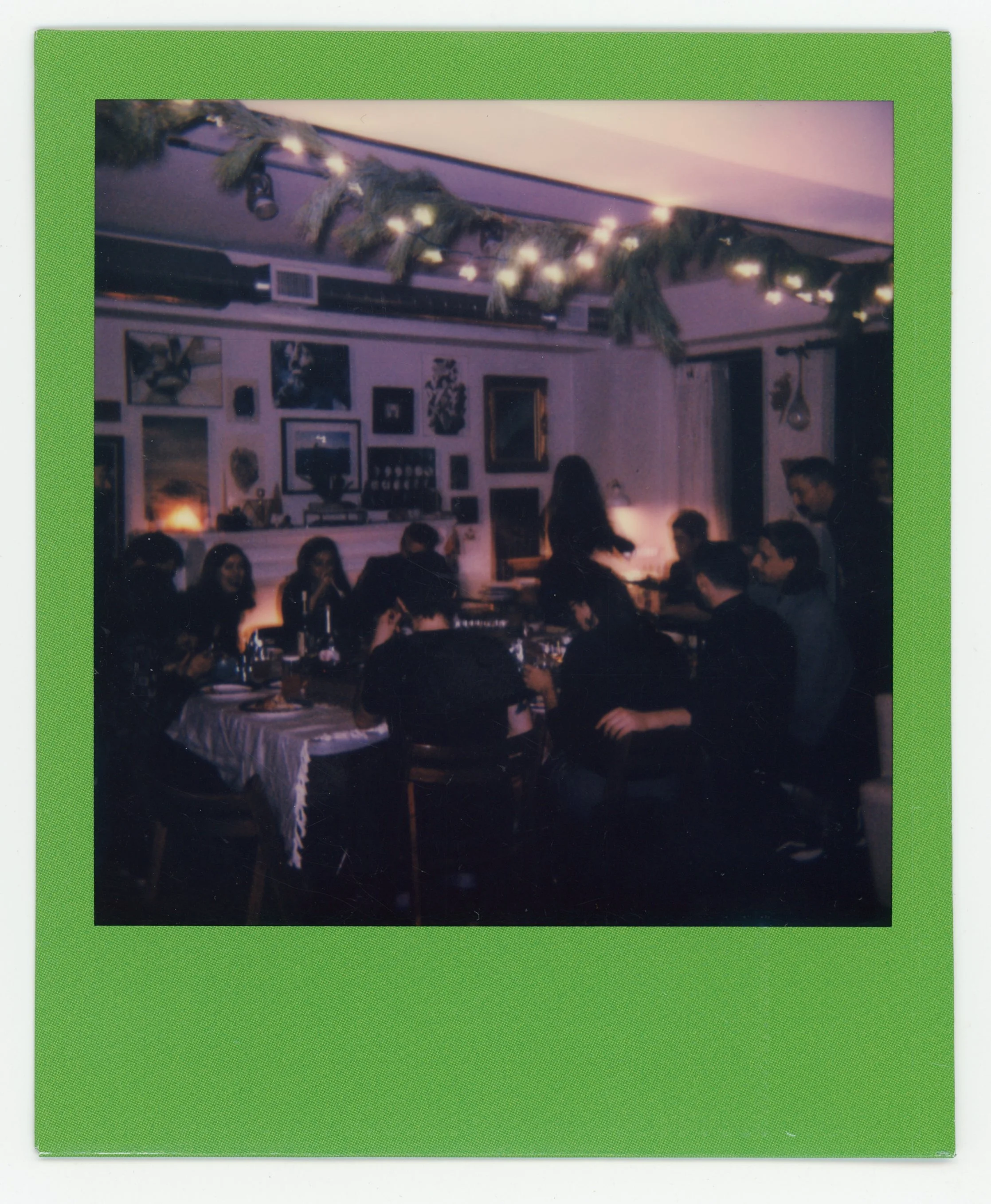 People gathered around a dining table for a meal in a decorated room with wall art and green garland with string lights hanging from the ceiling.