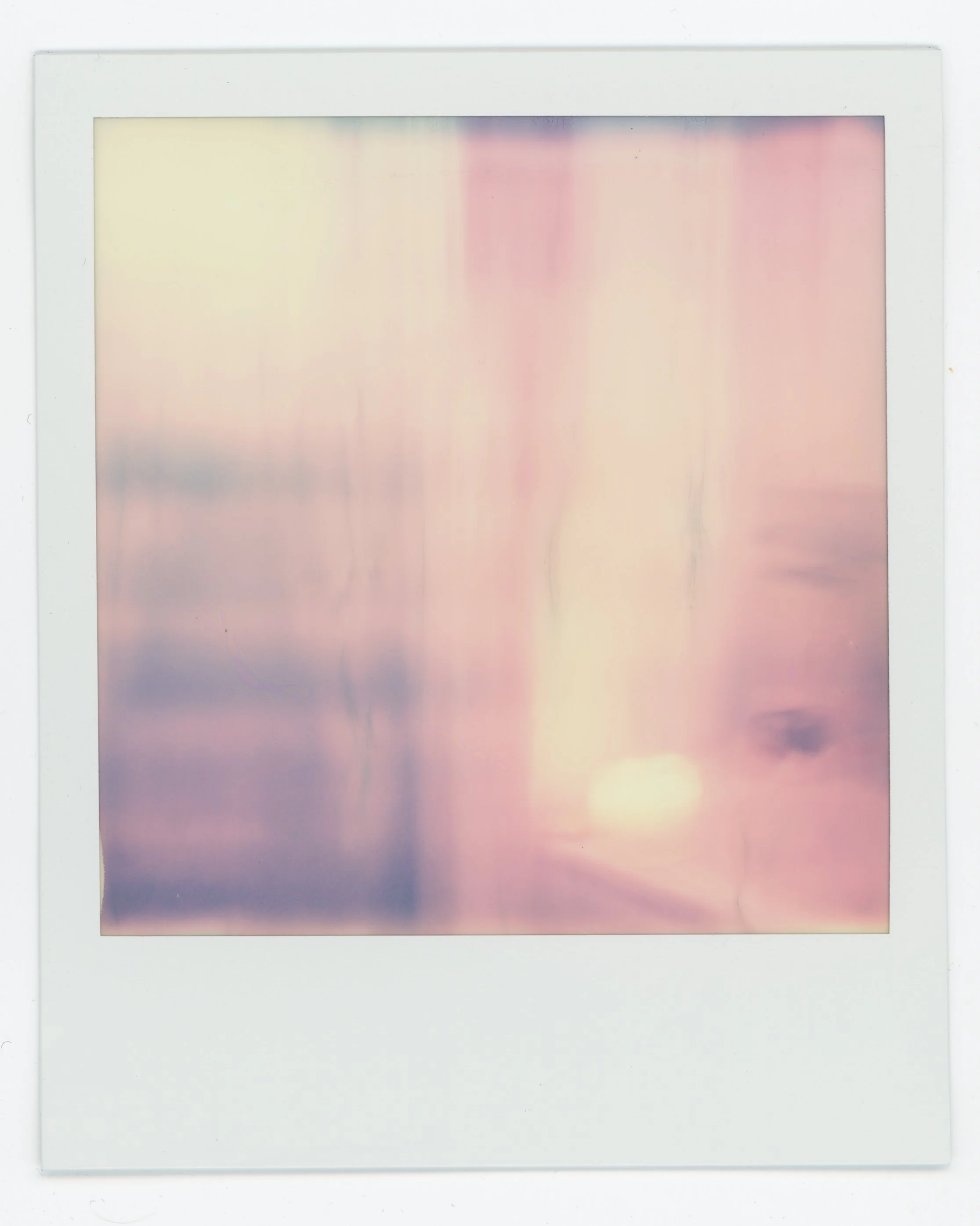 Abstract pastel-colored photograph with soft pink, purple, and yellow hues, resembling a blurred sunset or sunrise scene.