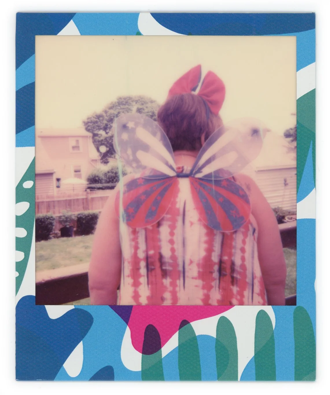 Person with butterfly costume wings and red bow headband facing away, standing outdoors in a backyard with houses and trees in the background.