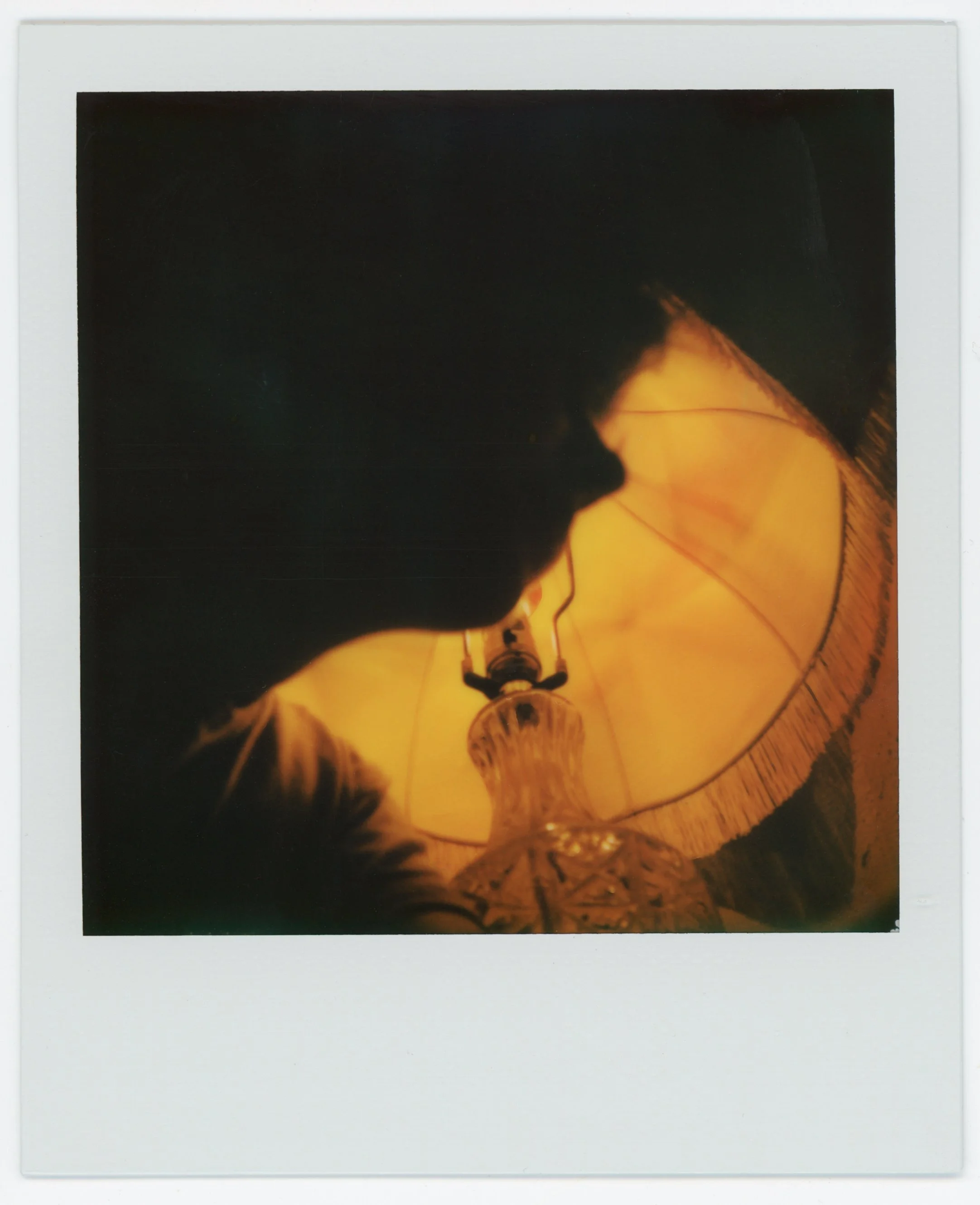 A person looking up at a glowing yellow lamp, seen from below, with the lamp's shade and ornate base visible.