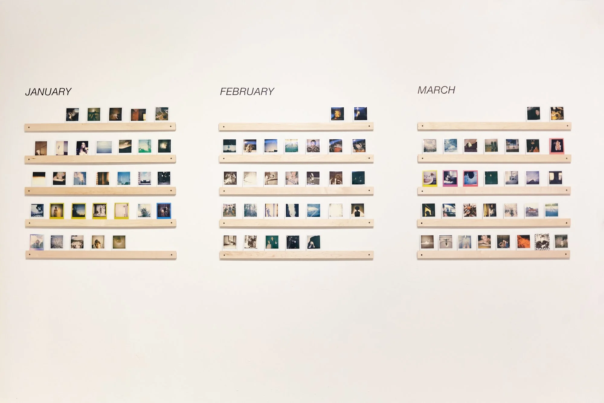 Wall display of photos organized by month: January, February, March, with wooden shelves holding small square photos.