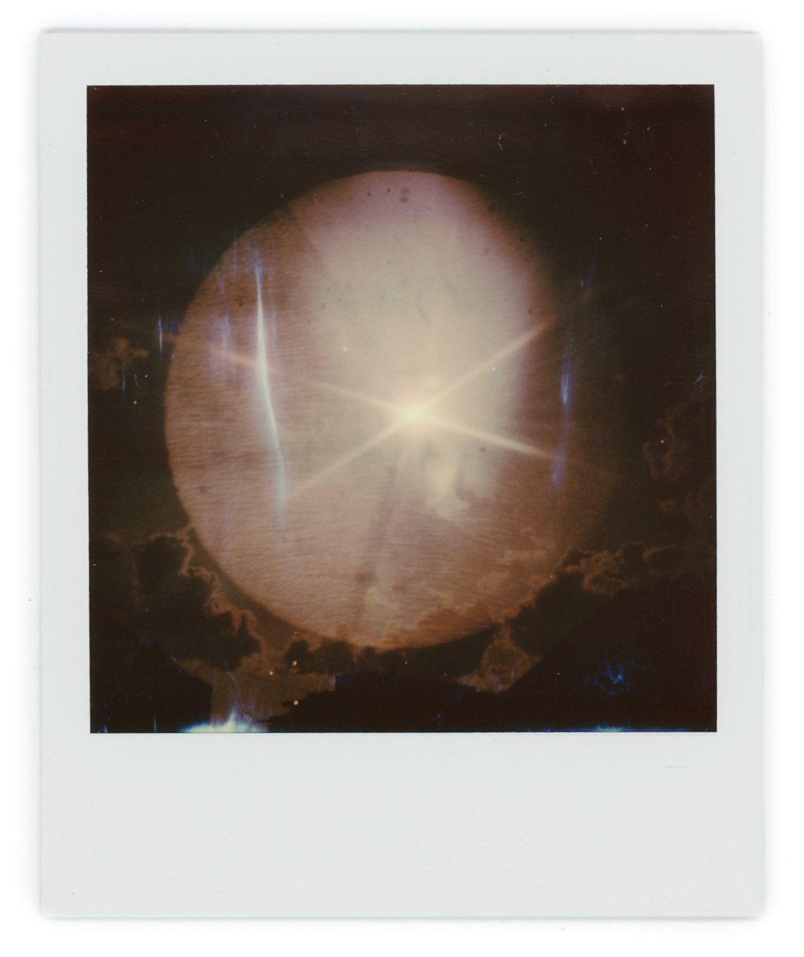 Polaroid photo of a glowing, spherical, translucent object resembling a planet or moon with bright light and starburst effects, surrounded by clouds.