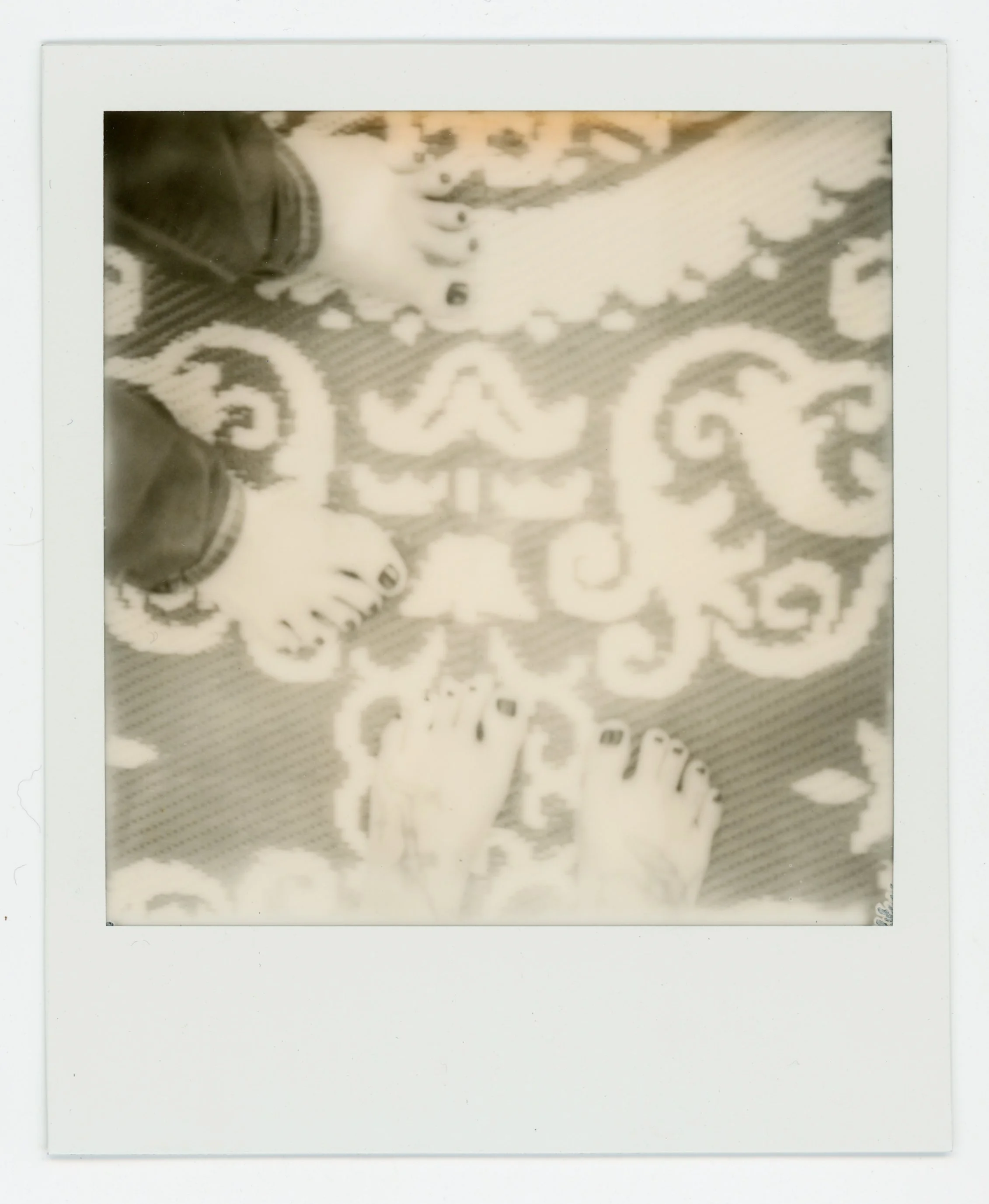 Polaroid photo of feet standing on a patterned rug.