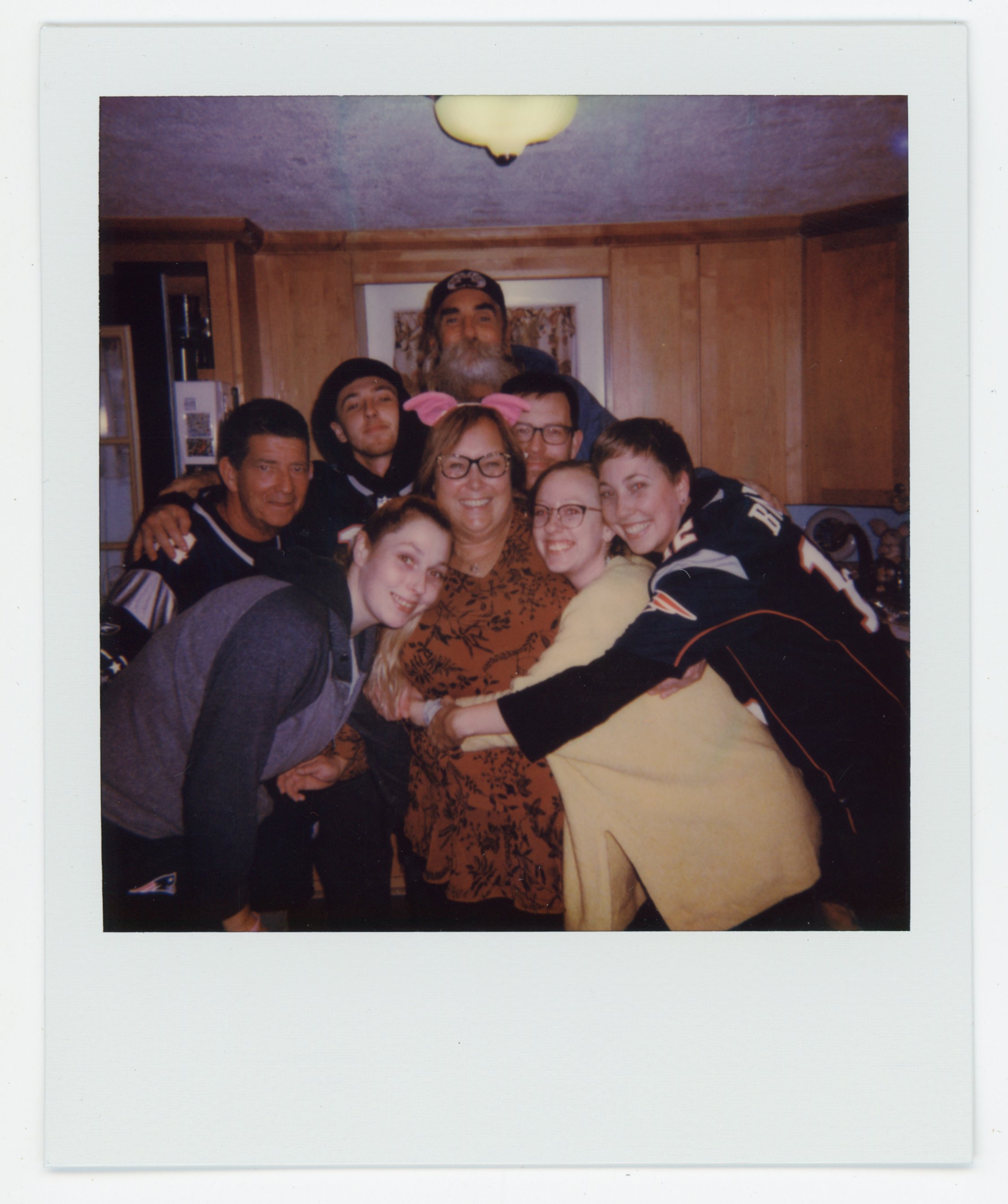 Group of people gathered together, smiling, in a cozy kitchen with wooden cabinets, celebrating a joyful moment.