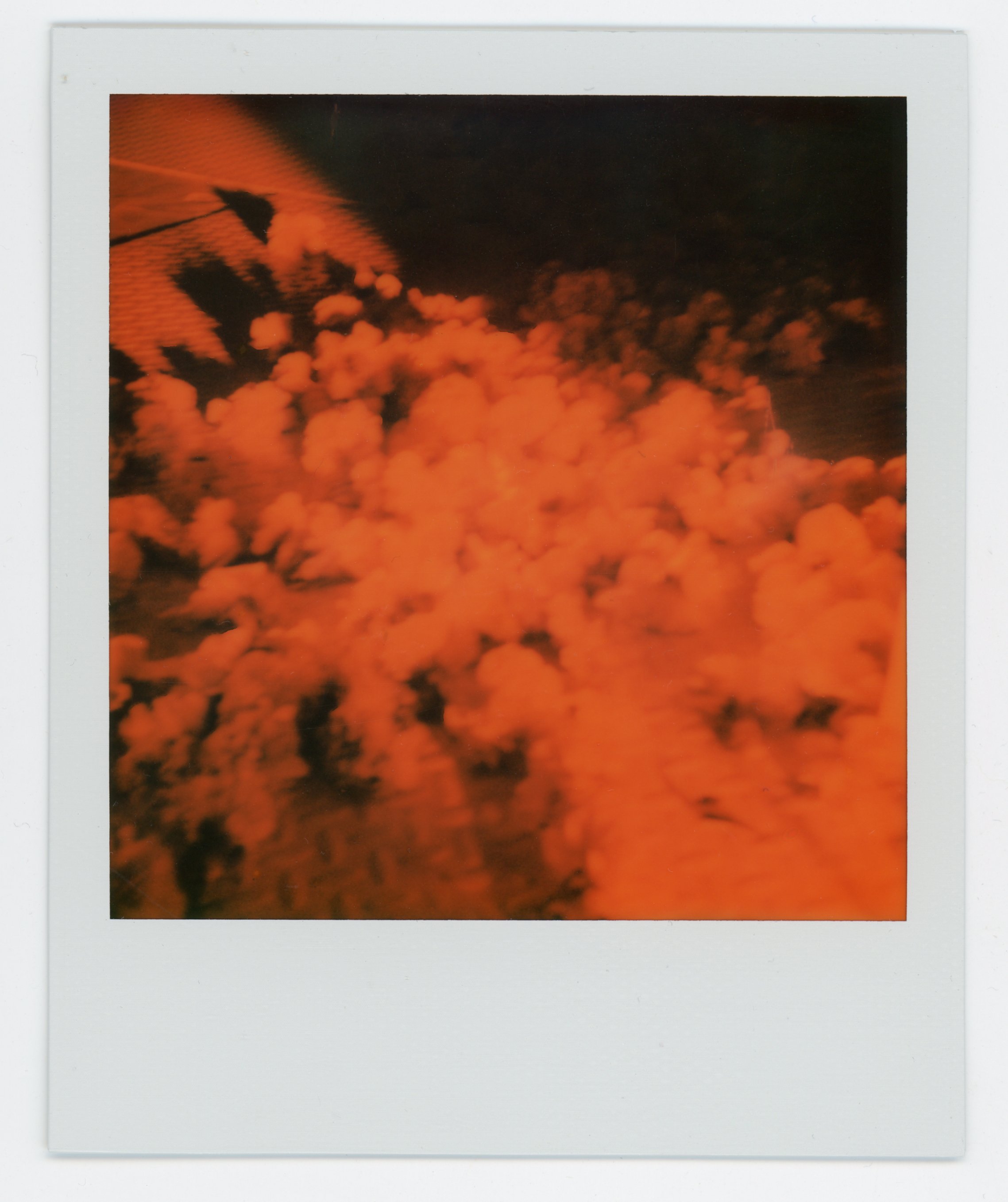 Orange smoke or vapor with a dark background and a shadow of a parachute or object at the top left corner.