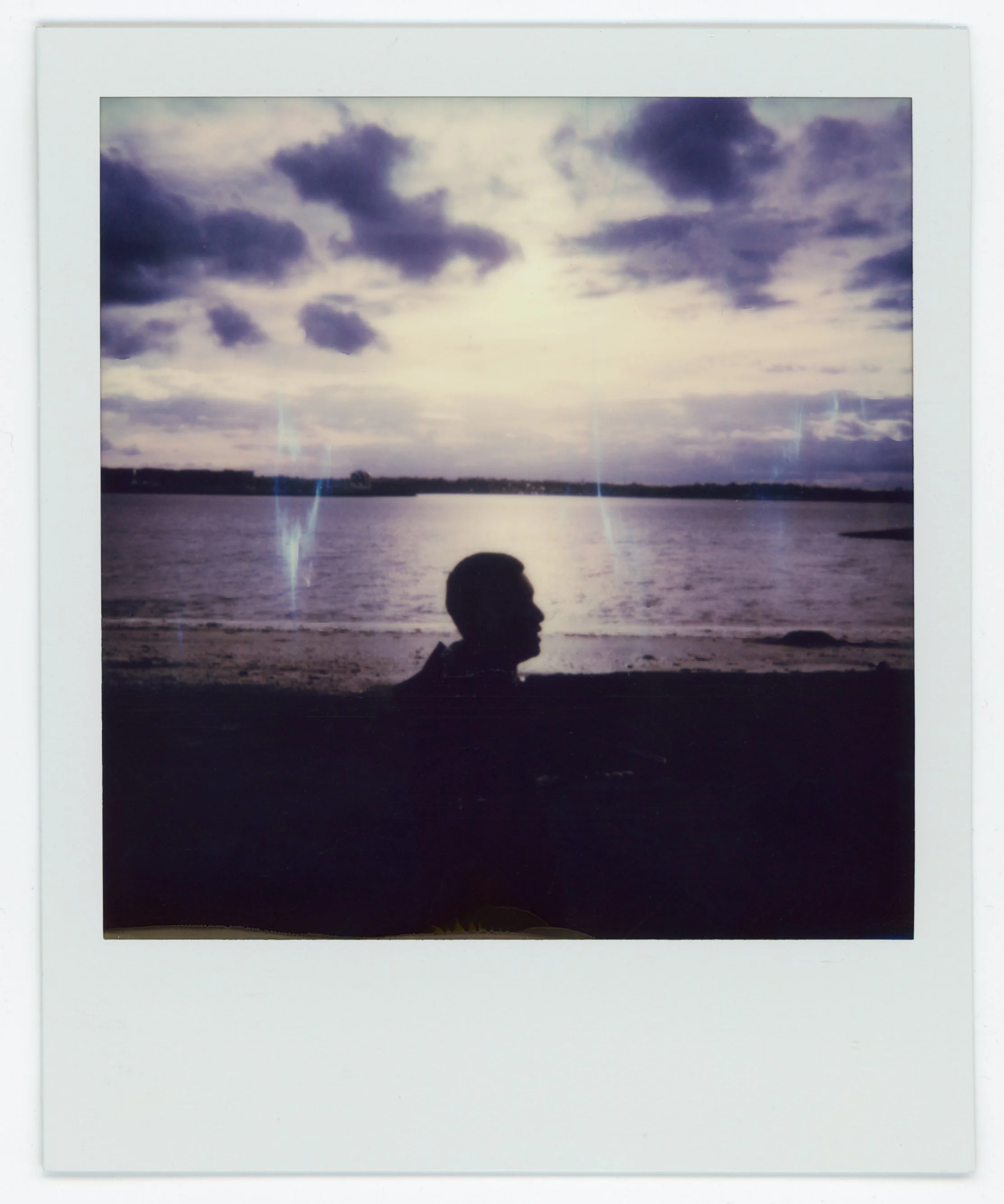 Silhouette of a person sitting on a beach with the ocean and a cloudy sky in the background.