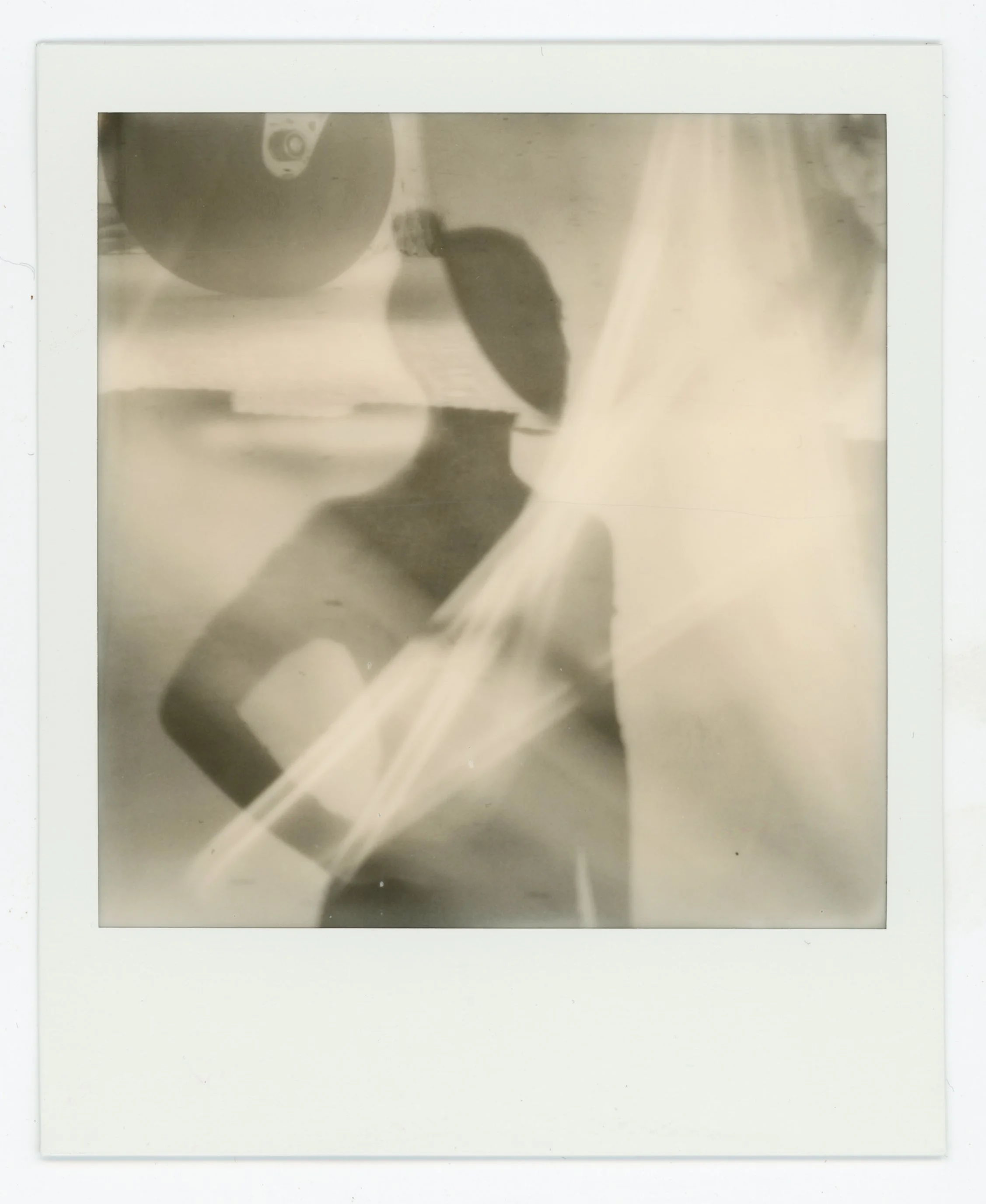 Black and white Polaroid photo showing a person in sunglasses and a hat, with abstract reflections and light streaks.