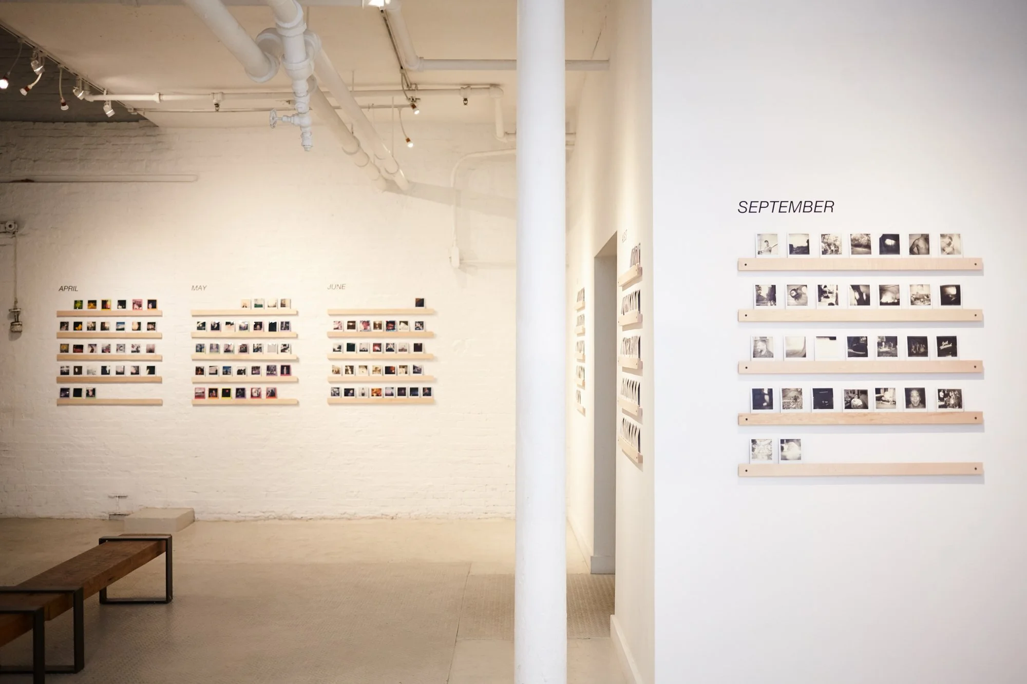 Gallery wall with monthly photo displays from April to September on wooden slats, arranged in rows on a white wall.