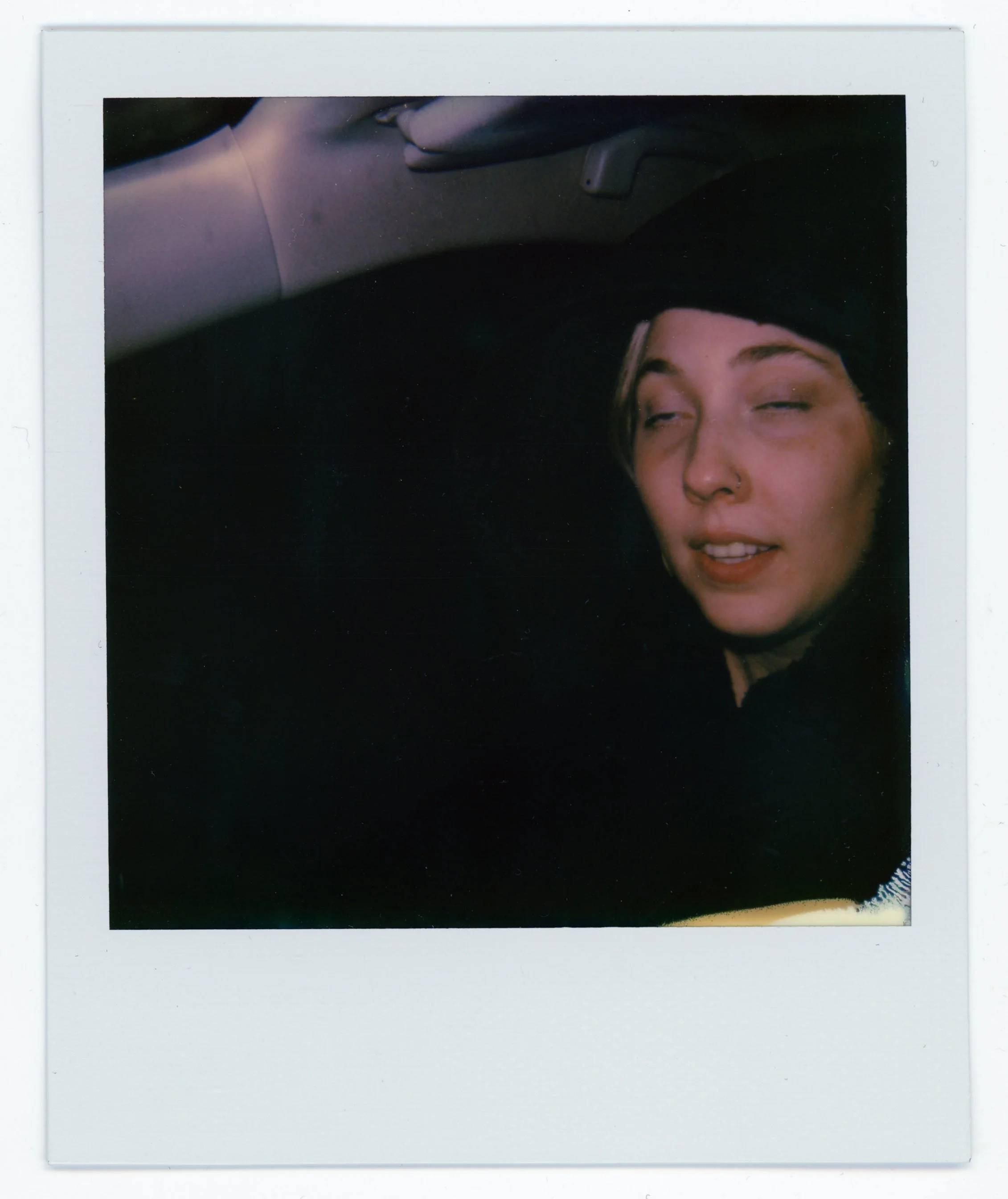 A woman with a black beanie and nose piercing making a funny face inside a car.