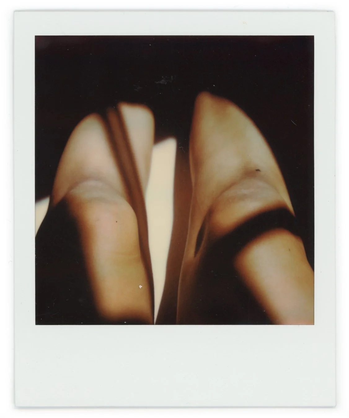 Polaroid photo of a person wearing beige pointed-toe high heels, viewed from above, with legs crossed