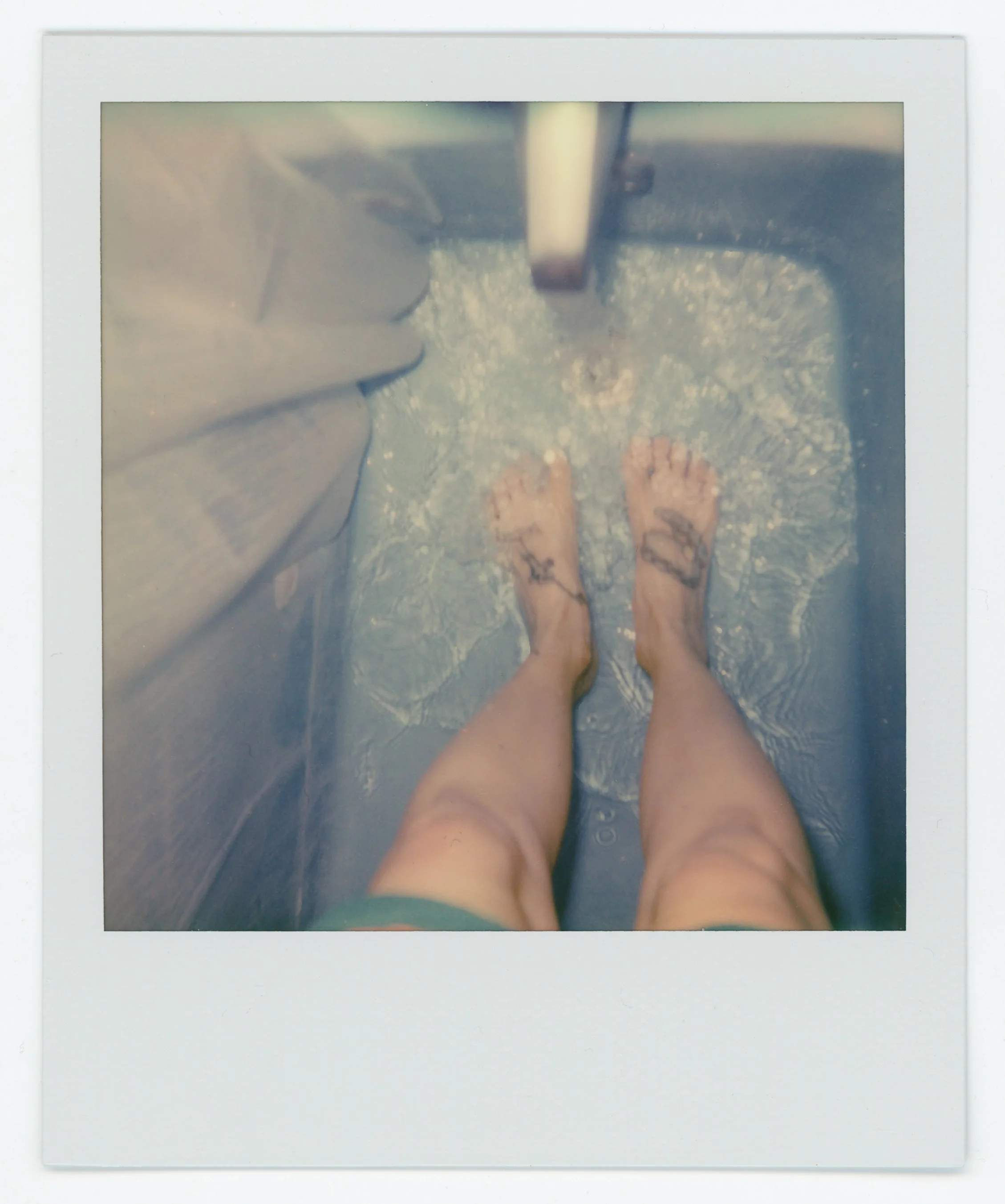 Person standing in a shower with water running, visible tattoos on their legs, view from above.