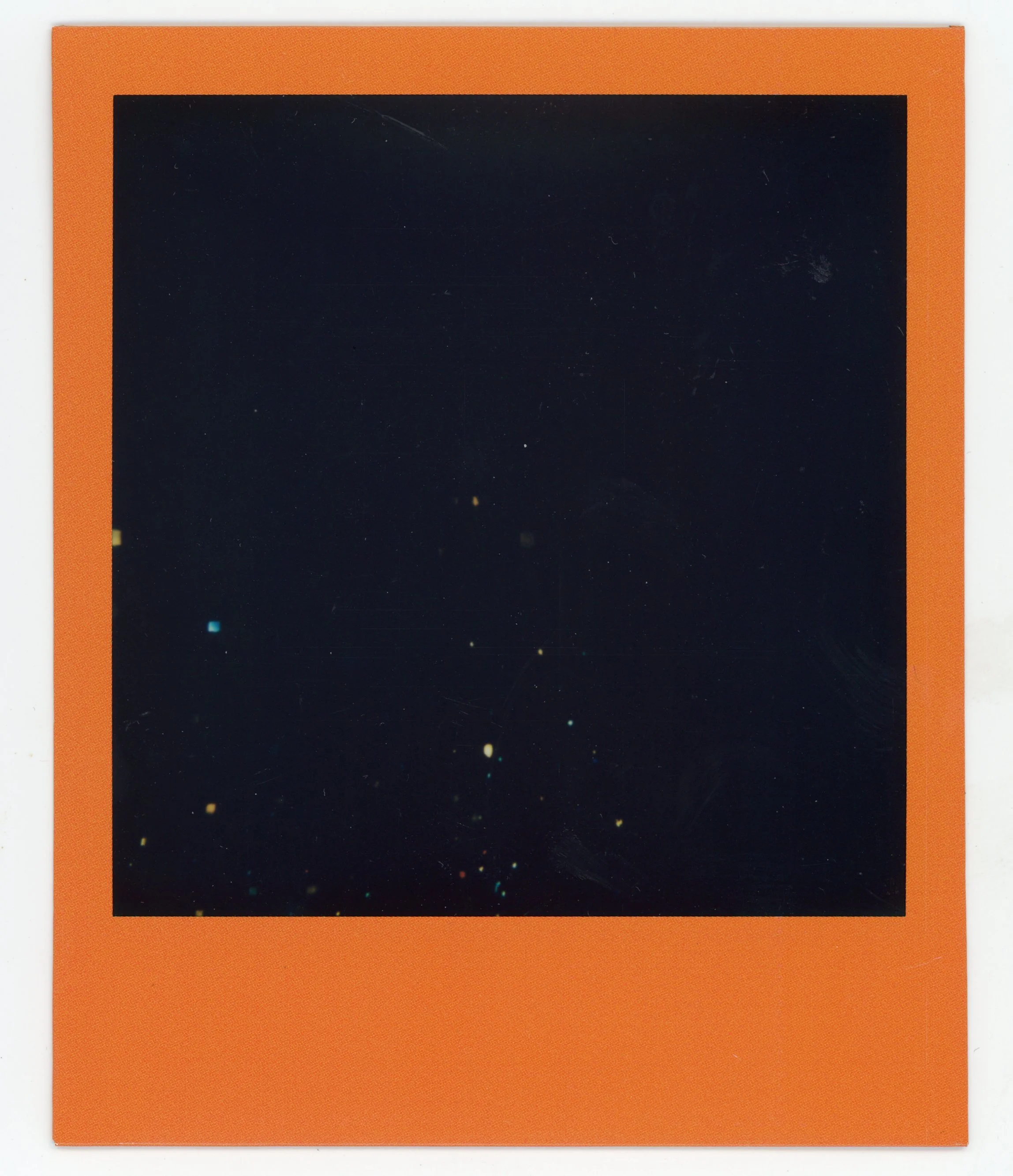 A blank instant film photo with an orange border, showing a black background with tiny specks resembling stars.