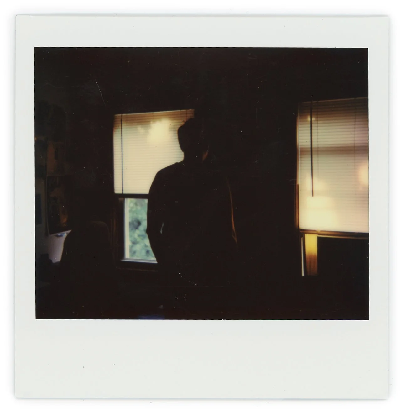 Silhouette of a person standing in front of two windows with closed blinds, backlit by daylight.