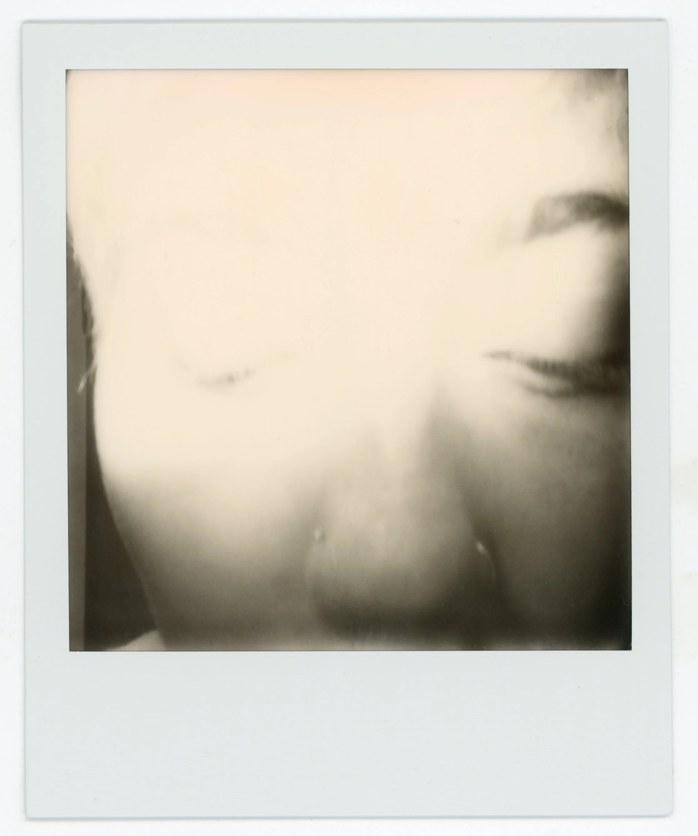 A Polaroid photo of a woman's face, blurred, with a focus on her lips and nose, partially obscured.