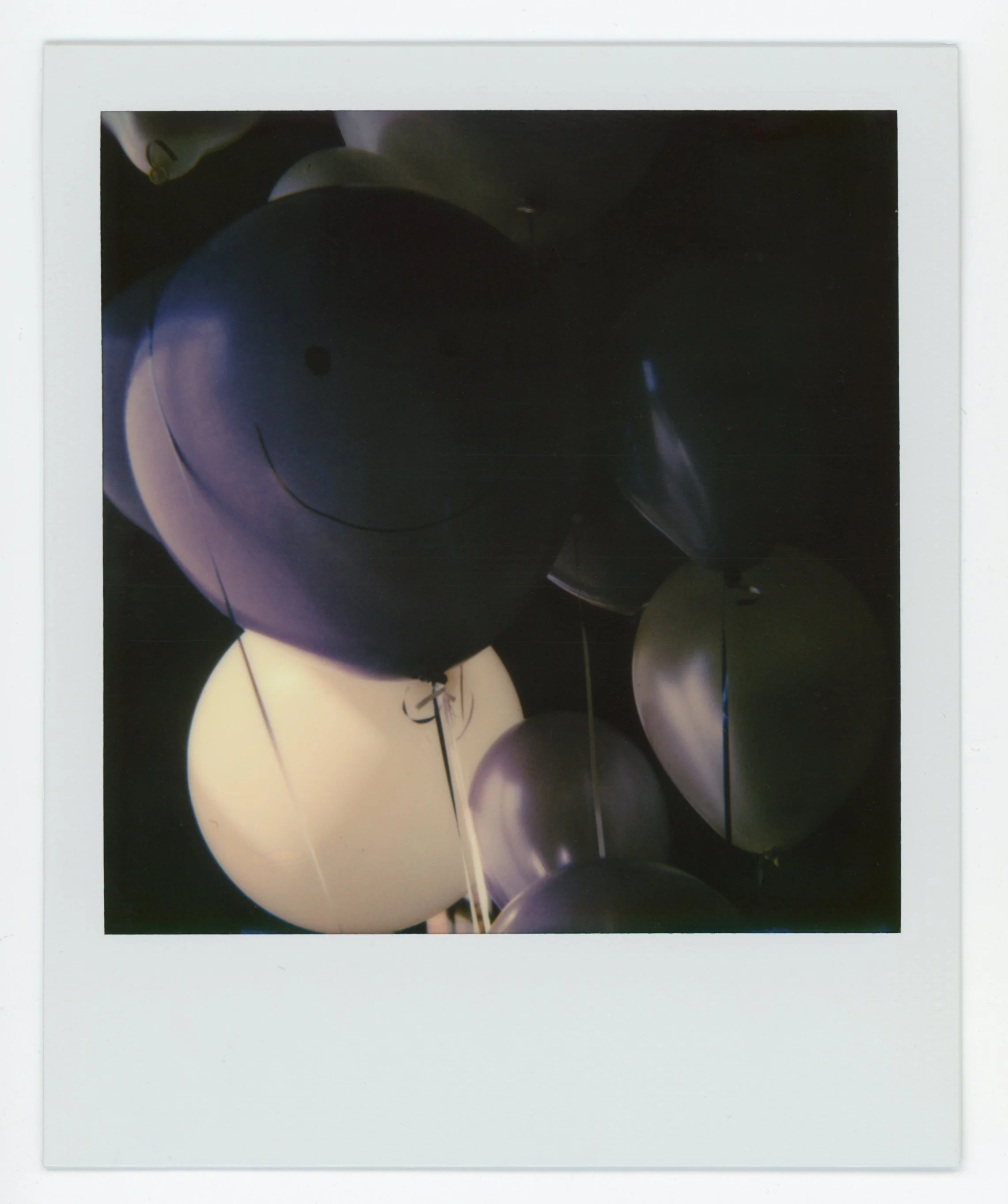 Polaroid photo of black, white, gold, and purple balloons with a smiley face on the black balloon.