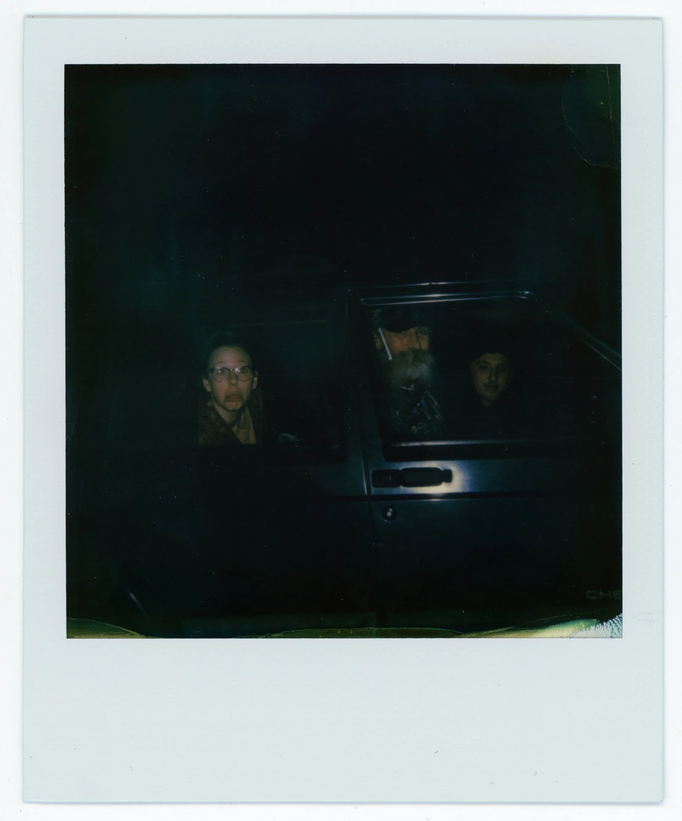 Three people sitting inside a dark vehicle, with one woman looking surprised or shocked.
