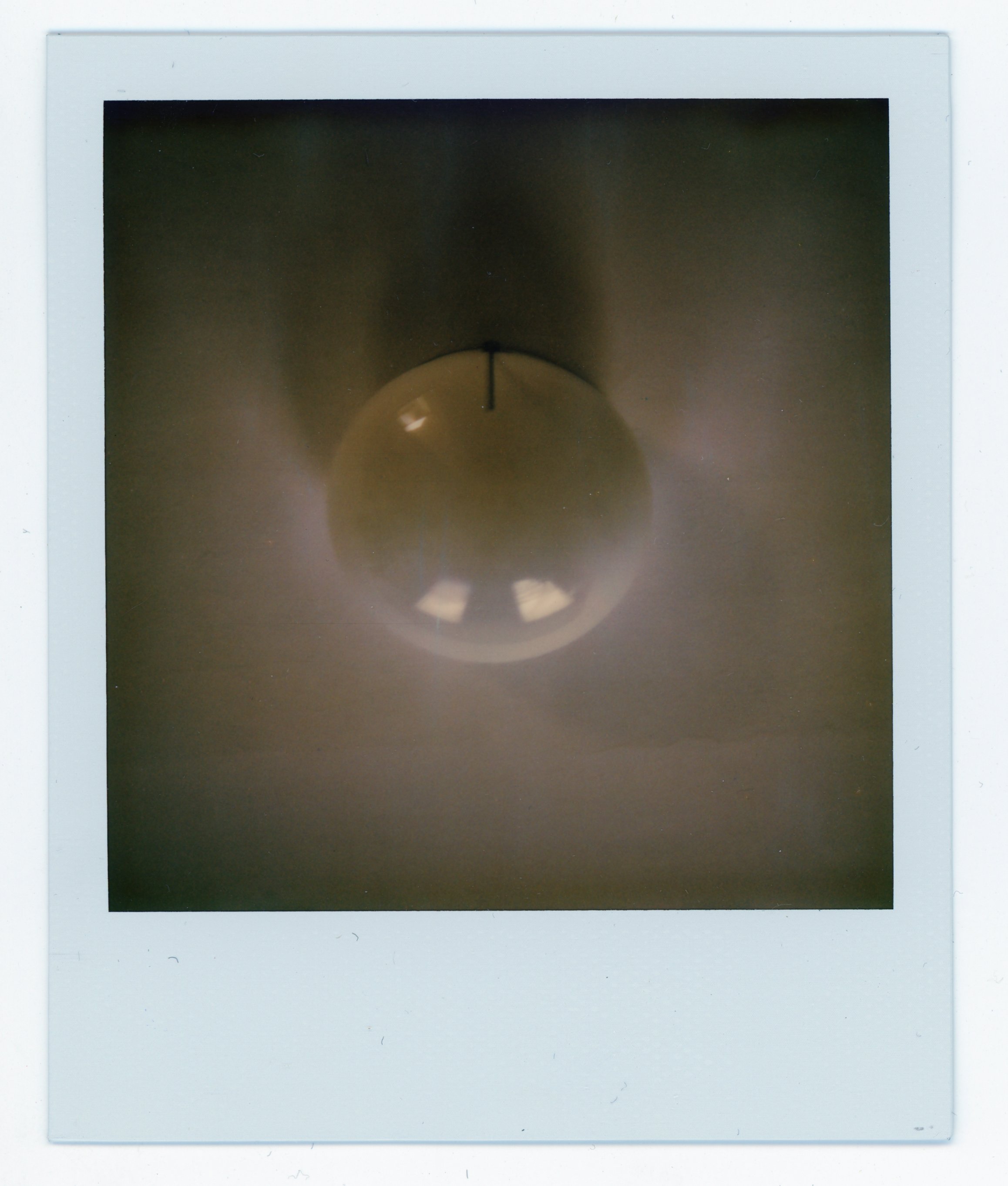 Close-up of a wall clock showing 12:00, taken through a reflective surface with a white border.