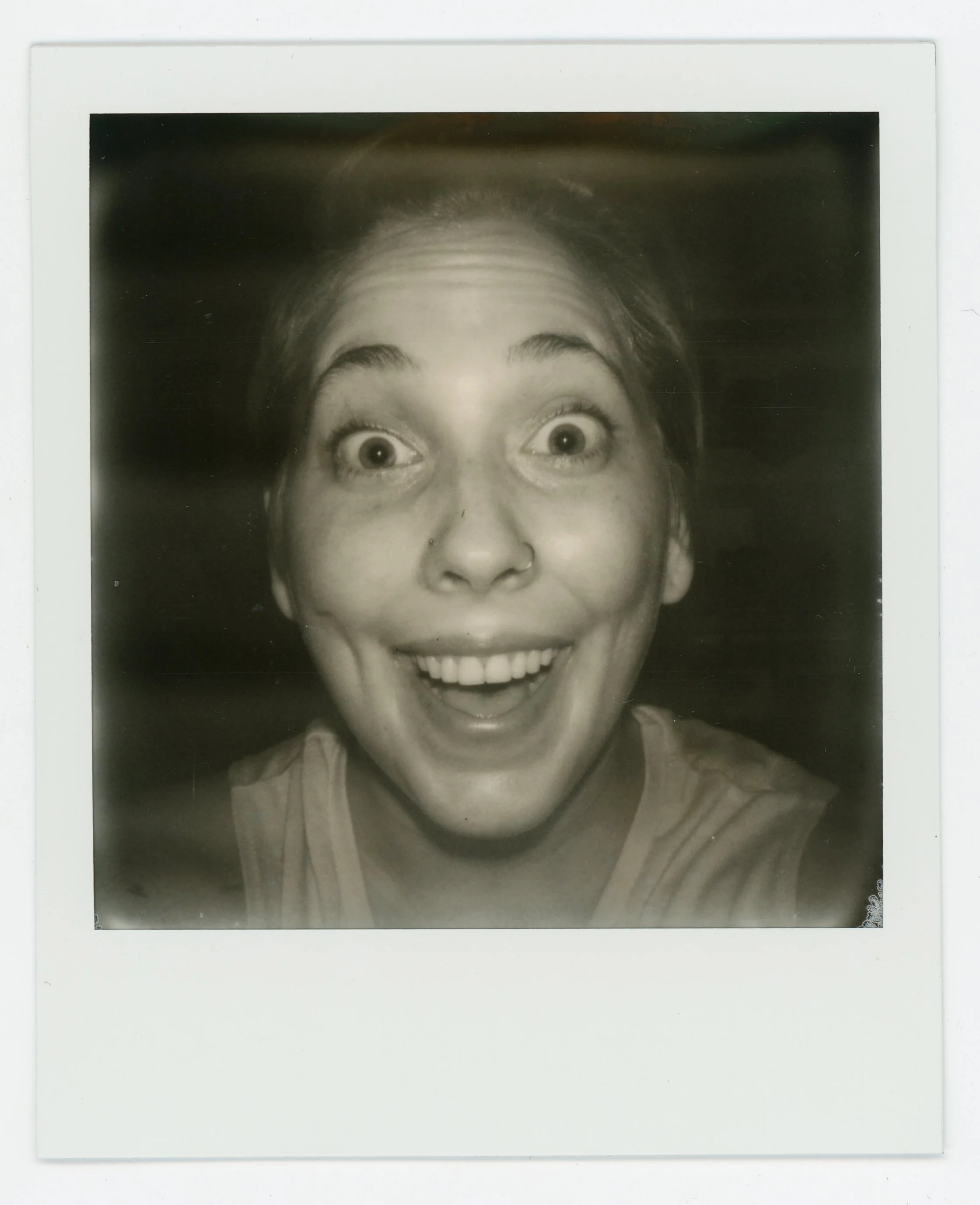 Black and white photo of a woman with an excited, wide-eyed smile, showing her teeth, and looking directly at the camera.