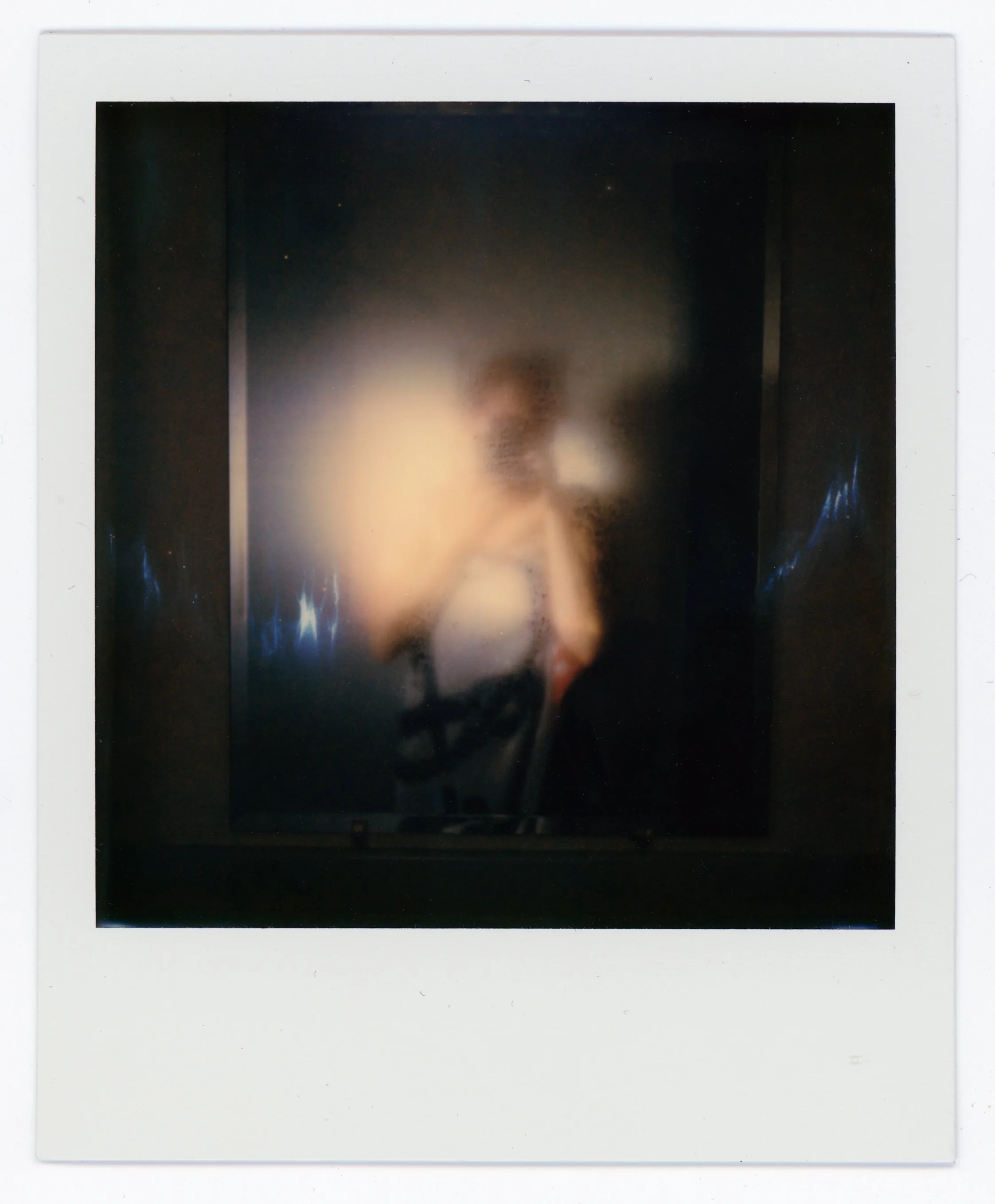 A blurry photo showing a face and upper body of a person with light-colored hair, possibly backlit or in motion, with some reflections or lights on either side of the image.