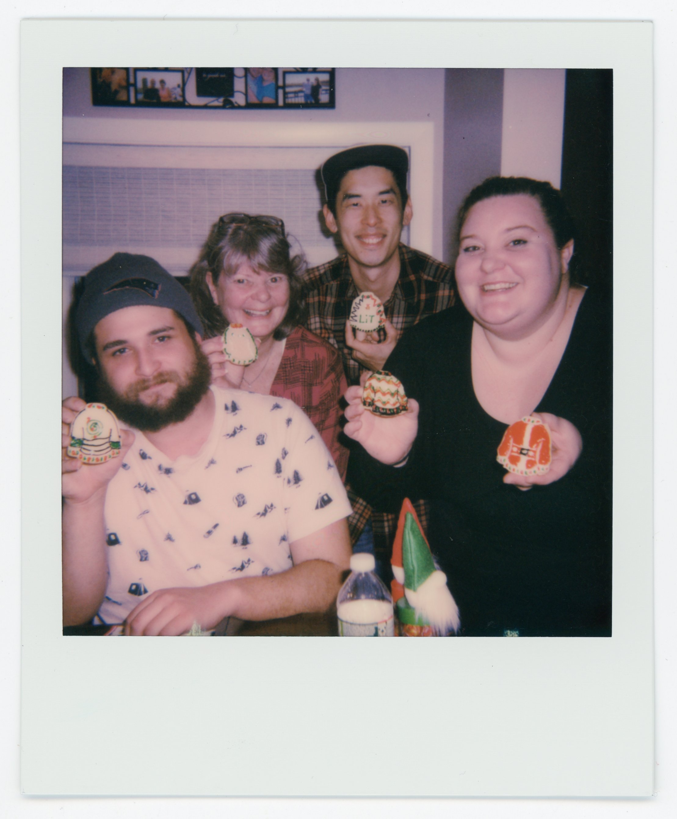 Group of five people celebrating with Christmas cookies, smiling at the camera, with holiday decorations in the background.