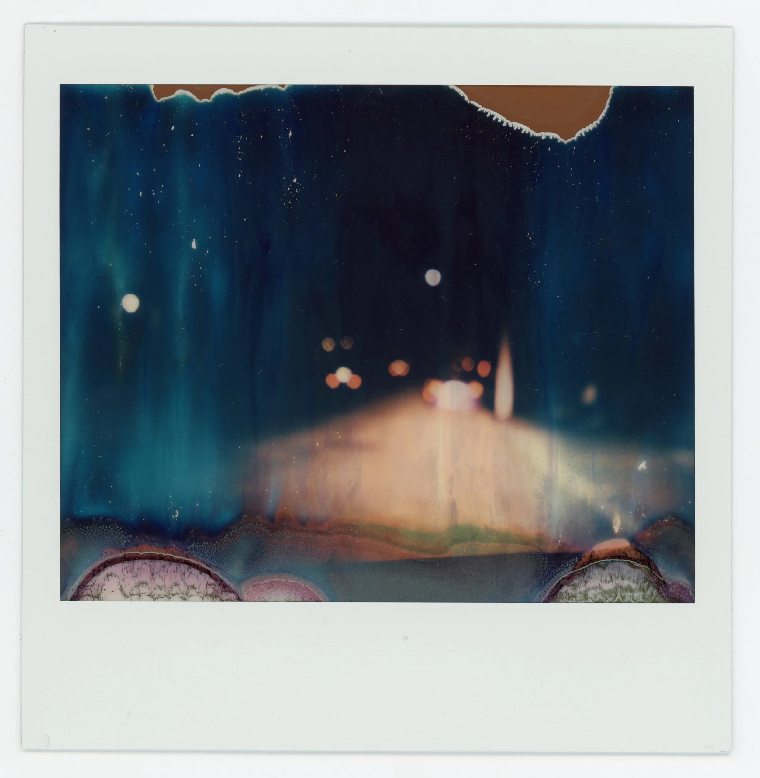 Polaroid photo of a blurry night scene with city lights and a street, featuring abstract shapes and colors.