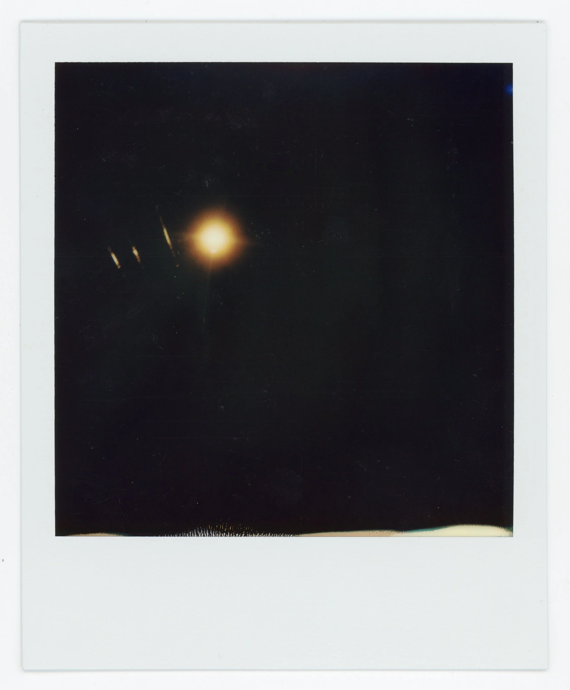 A blurry photograph of a bright light source against a dark background with some streaks of light and a faint horizon line at the bottom.