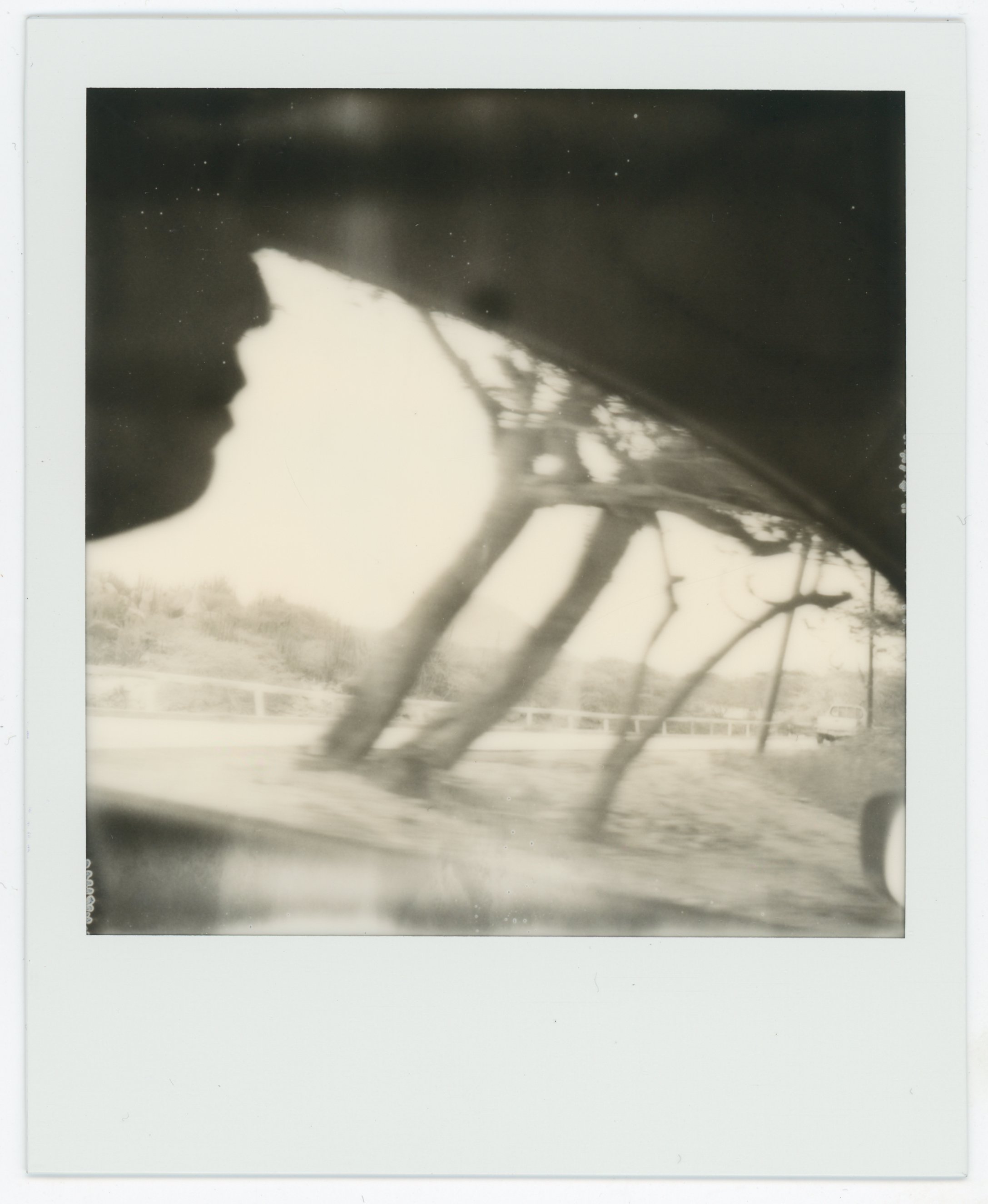 Black-and-white photo of a car's side mirror showing a distorted view of a road and landscape behind the vehicle.