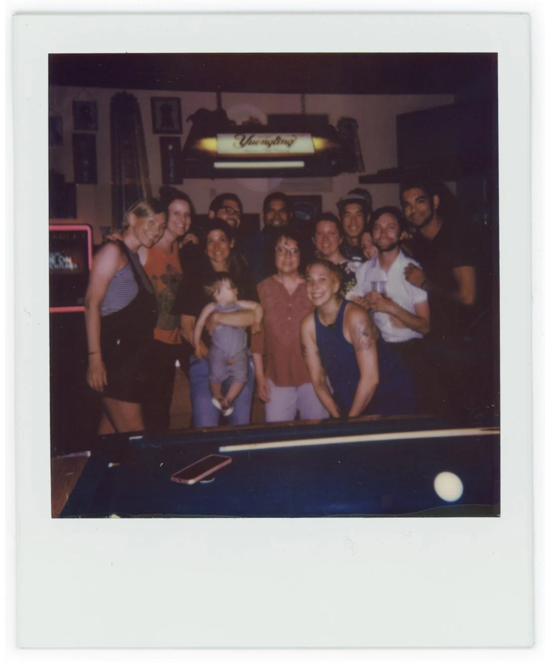 Group of people posing together in a bar or pub, some smiling, with a pool table and a sign that reads "Yardhouse" in the background.
