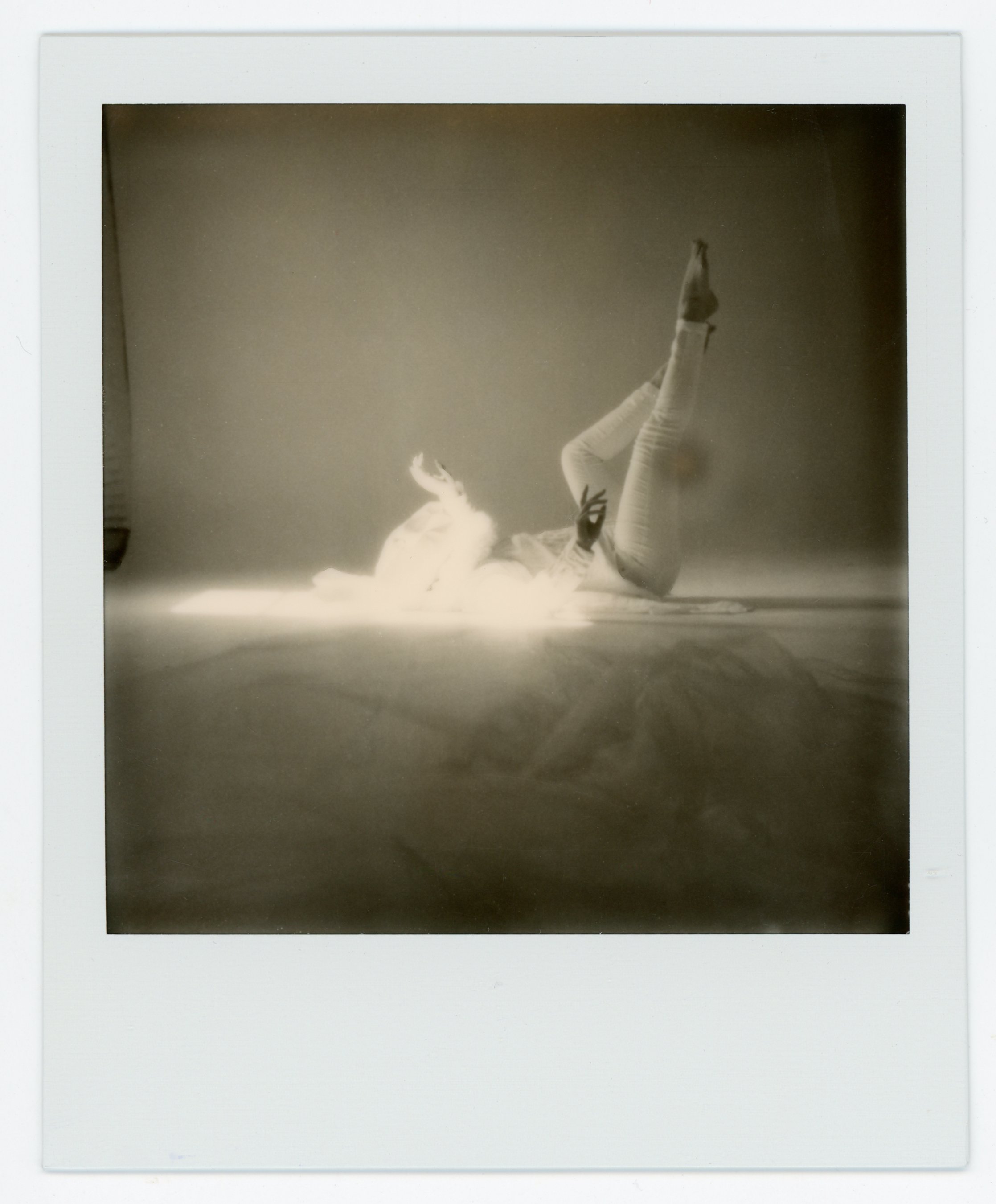 A person lying on the ground with legs raised and one hand forming an 'OK' sign, captured in black and white.