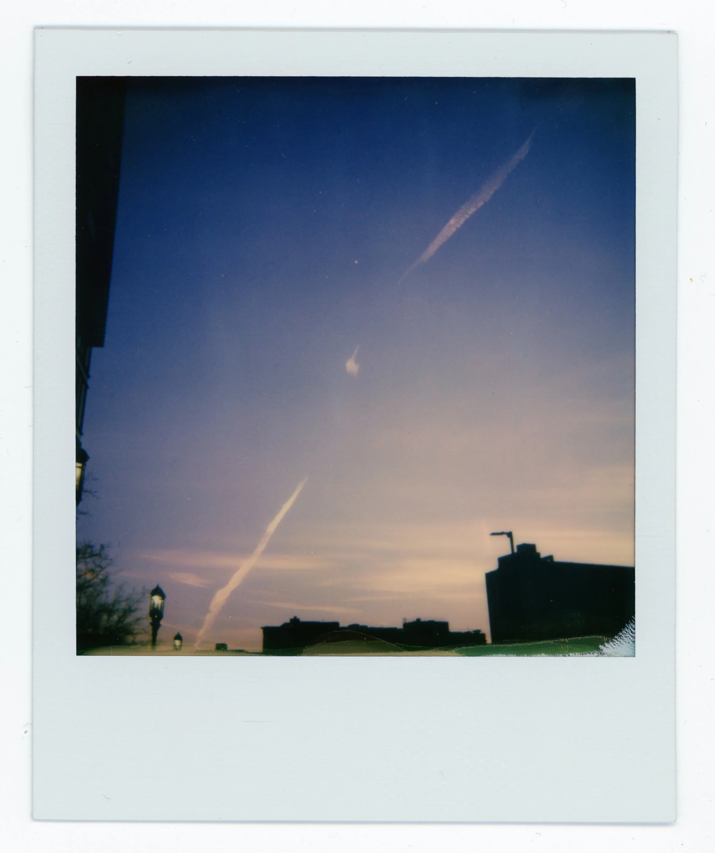Sky during sunset with contrails and buildings in silhouette