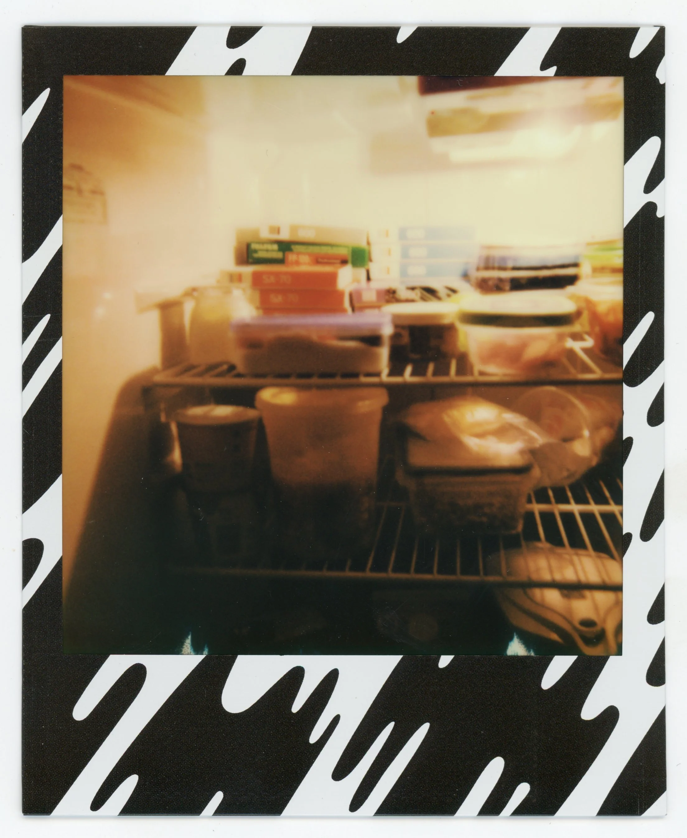 Open refrigerator with various food containers, boxes, and snacks on shelves, with a black and white patterned border around the photo.