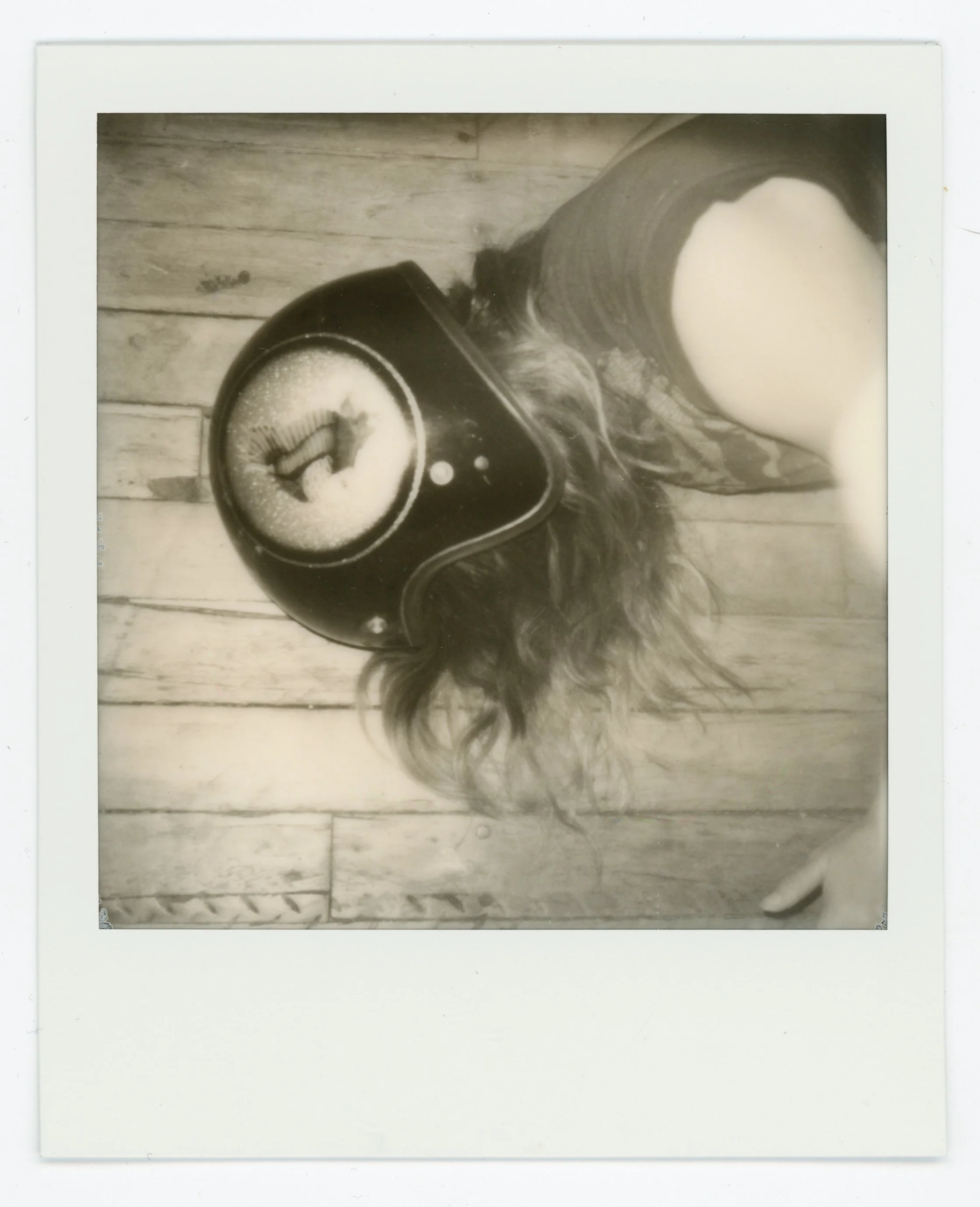 A person wearing a helmet with a fish design and long hair, standing on a wooden floor, with part of their arm visible, taking a photo from above.