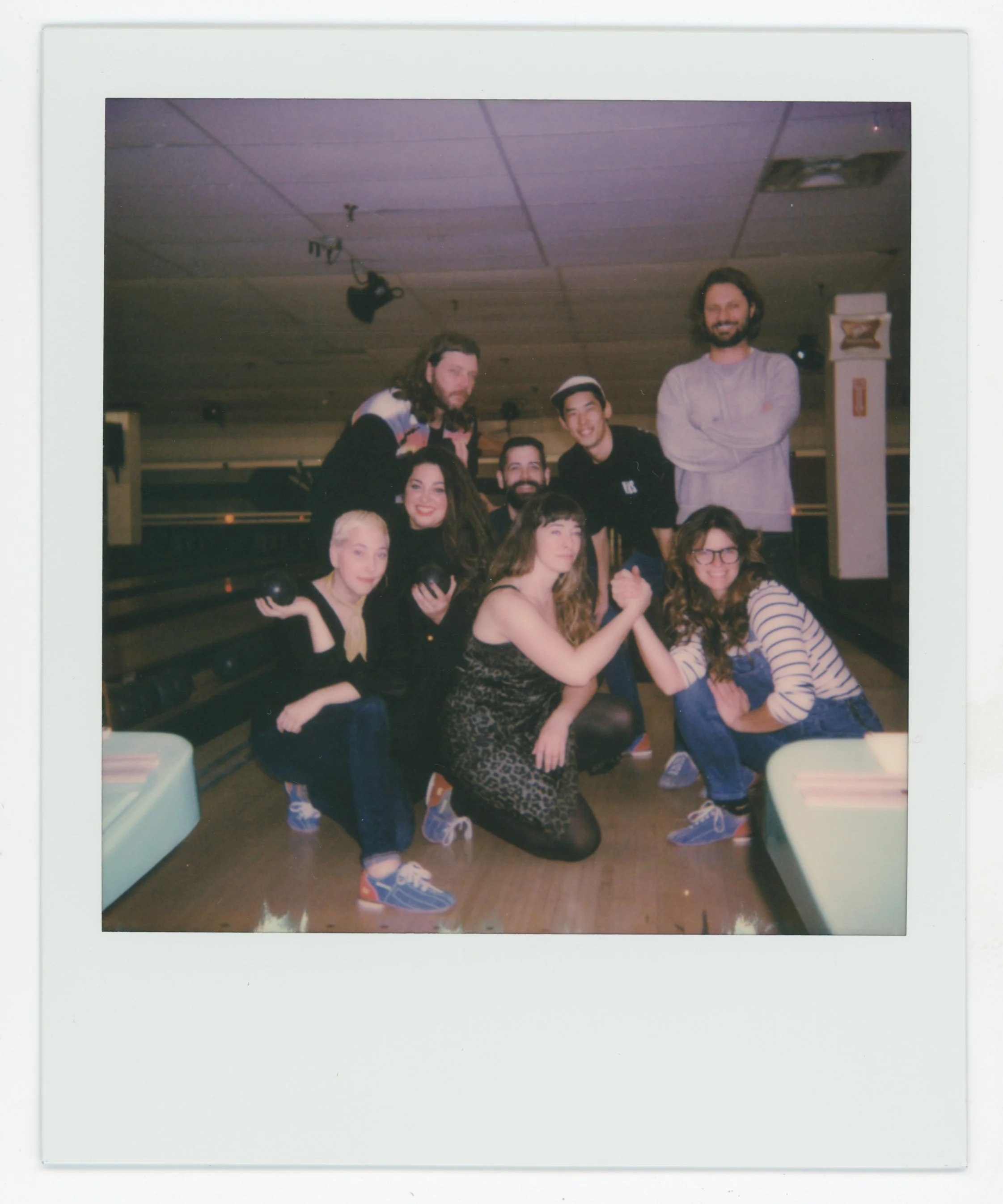 A group of nine people at a bowling alley, with some kneeling and others standing, celebrating.