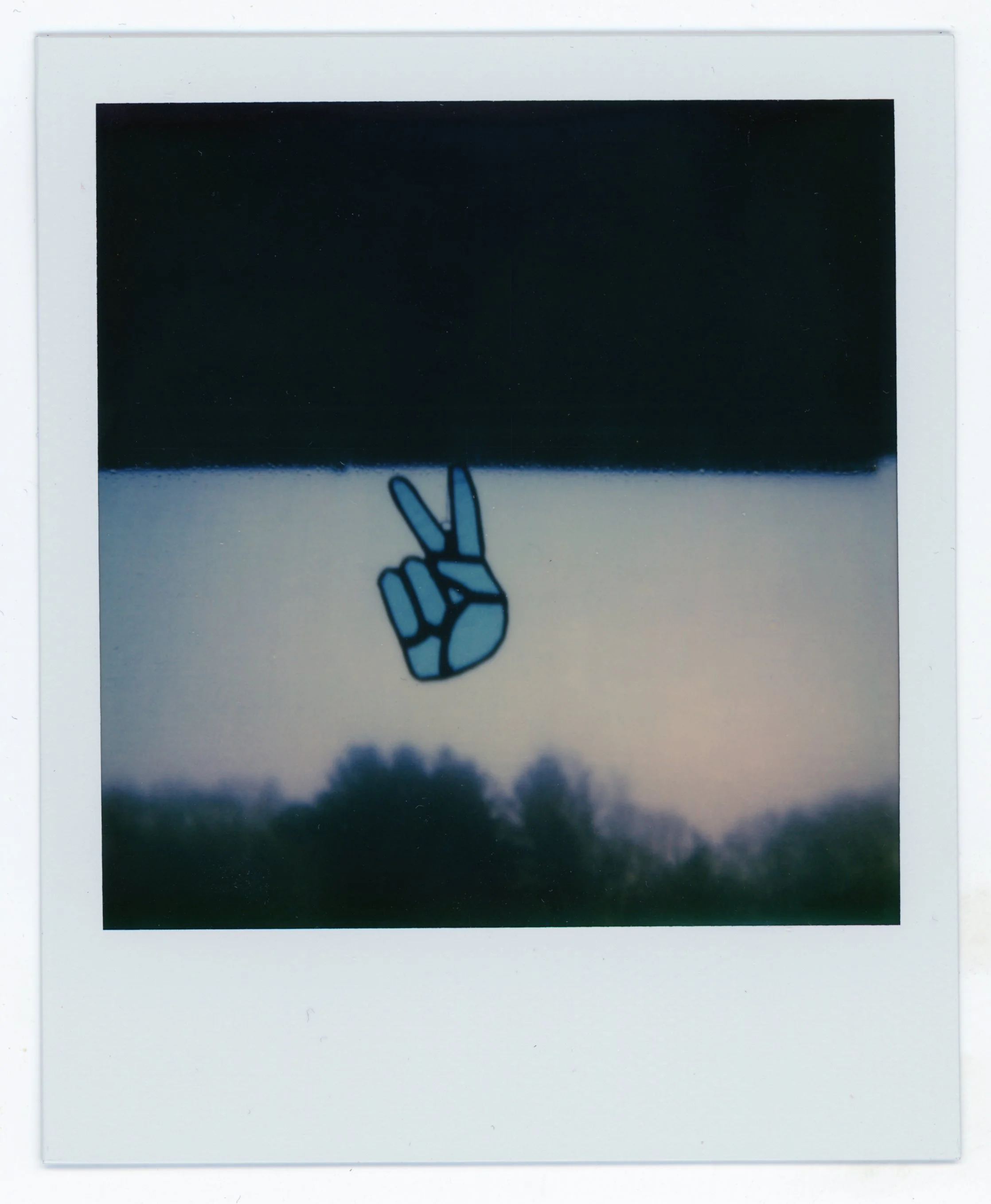 A peace sign sticker on a window with a blurry landscape of trees and sky in the background.