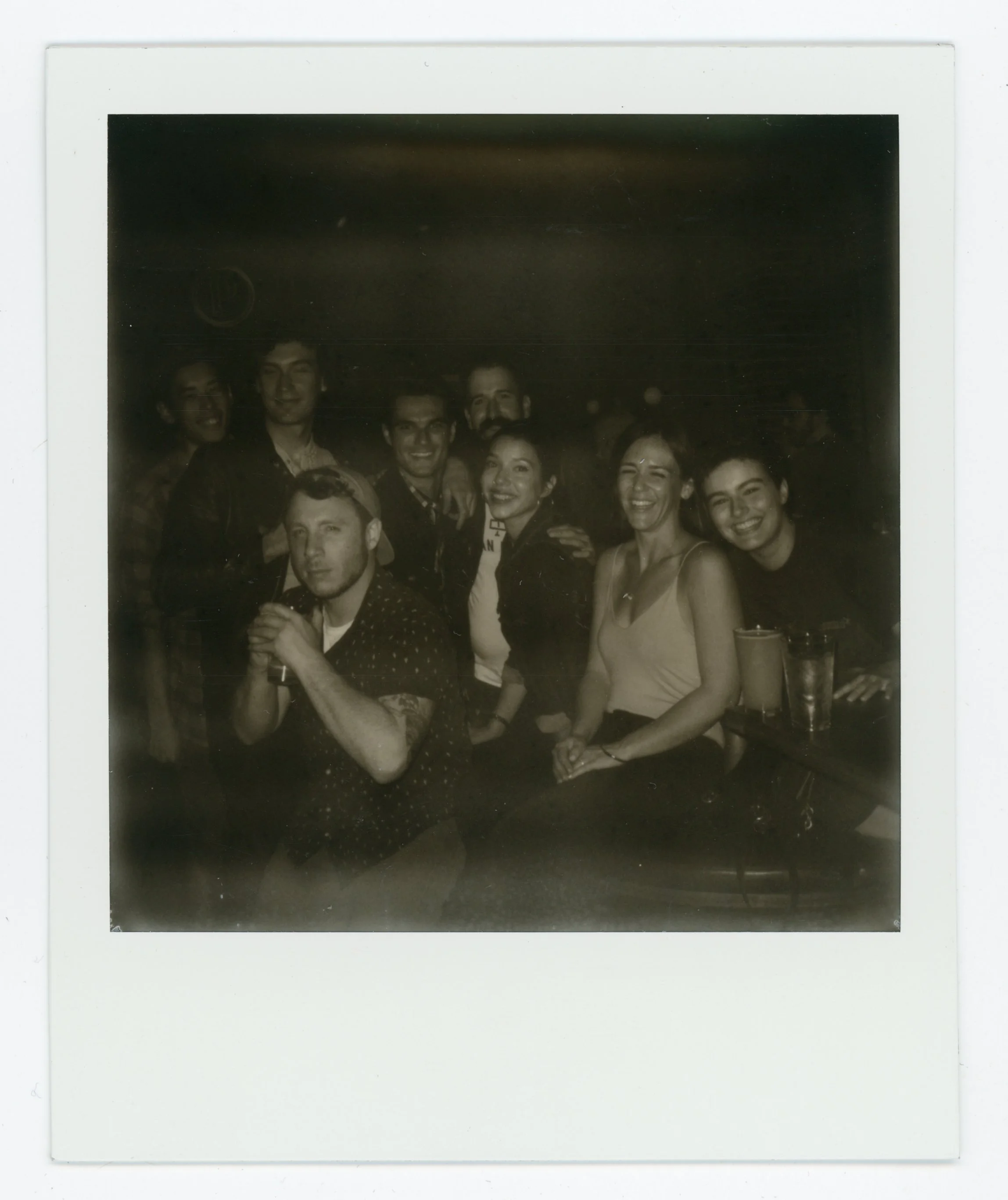 A group of nine people gathered together indoors for a social occasion, posing for a photo, some smiling and others with neutral expressions.