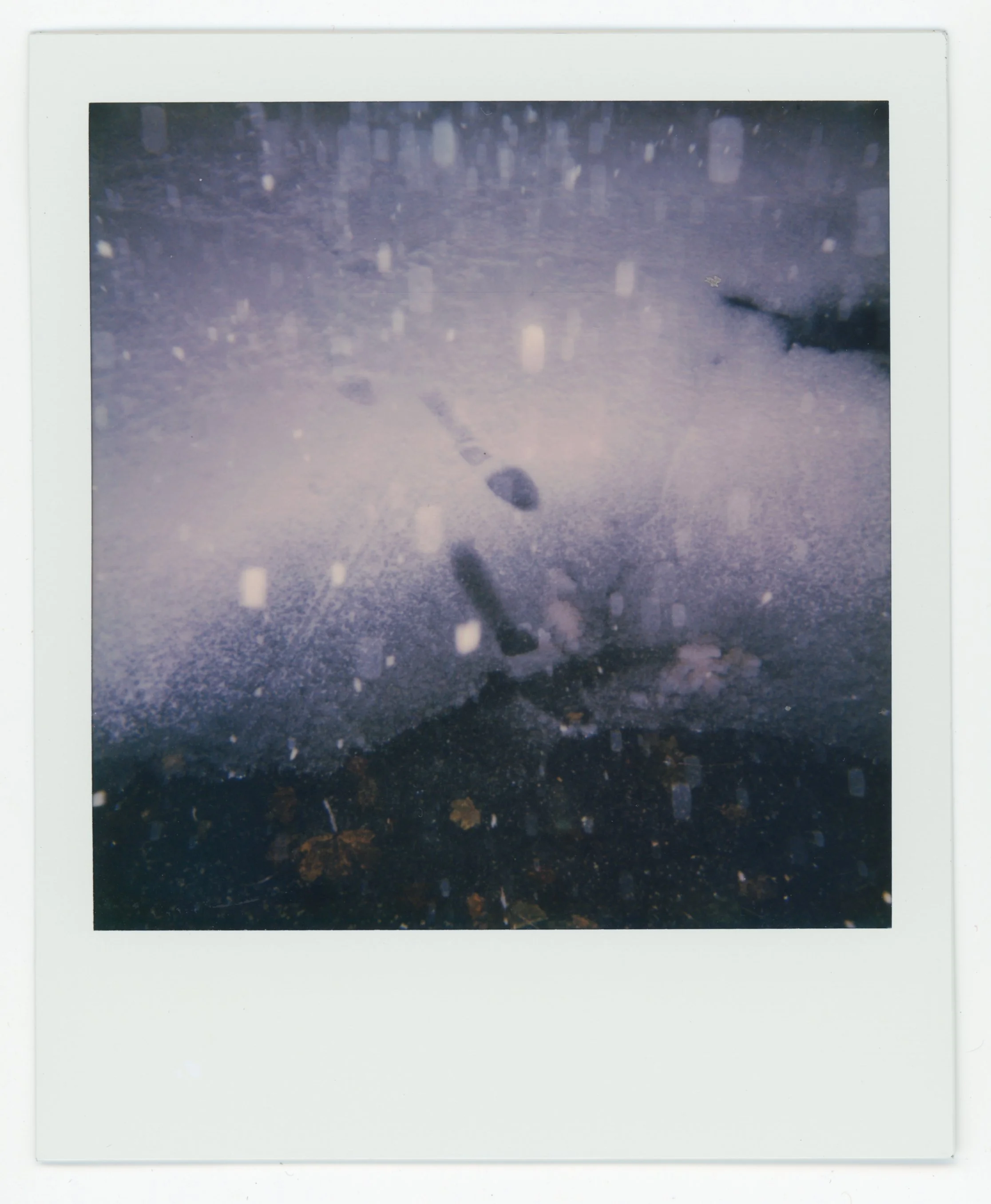 A snow-covered airplane crash site with debris scattered on the snow, framed in a white border, resembling a Polaroid photograph.