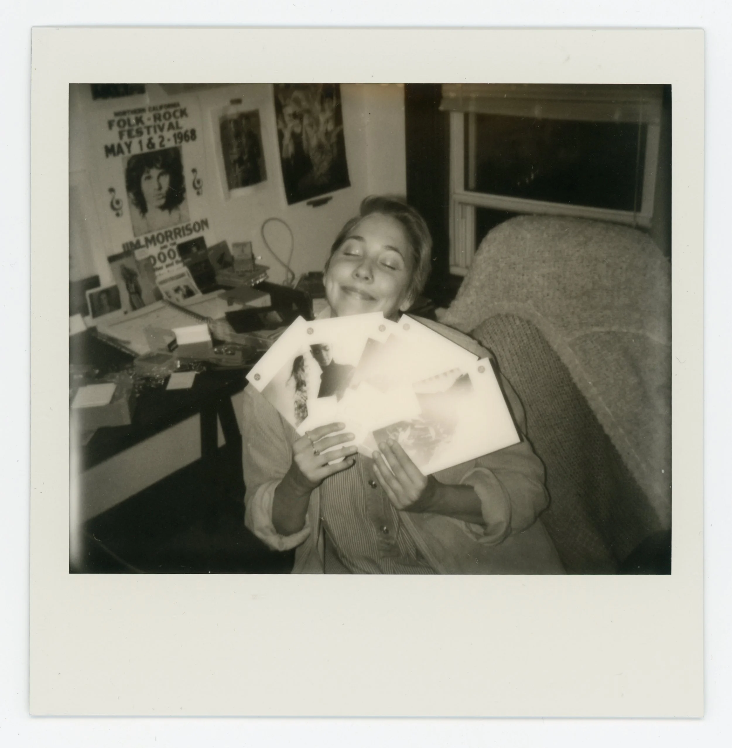 A woman smiling and holding several vinyl records in a room with posters and books on the wall.
