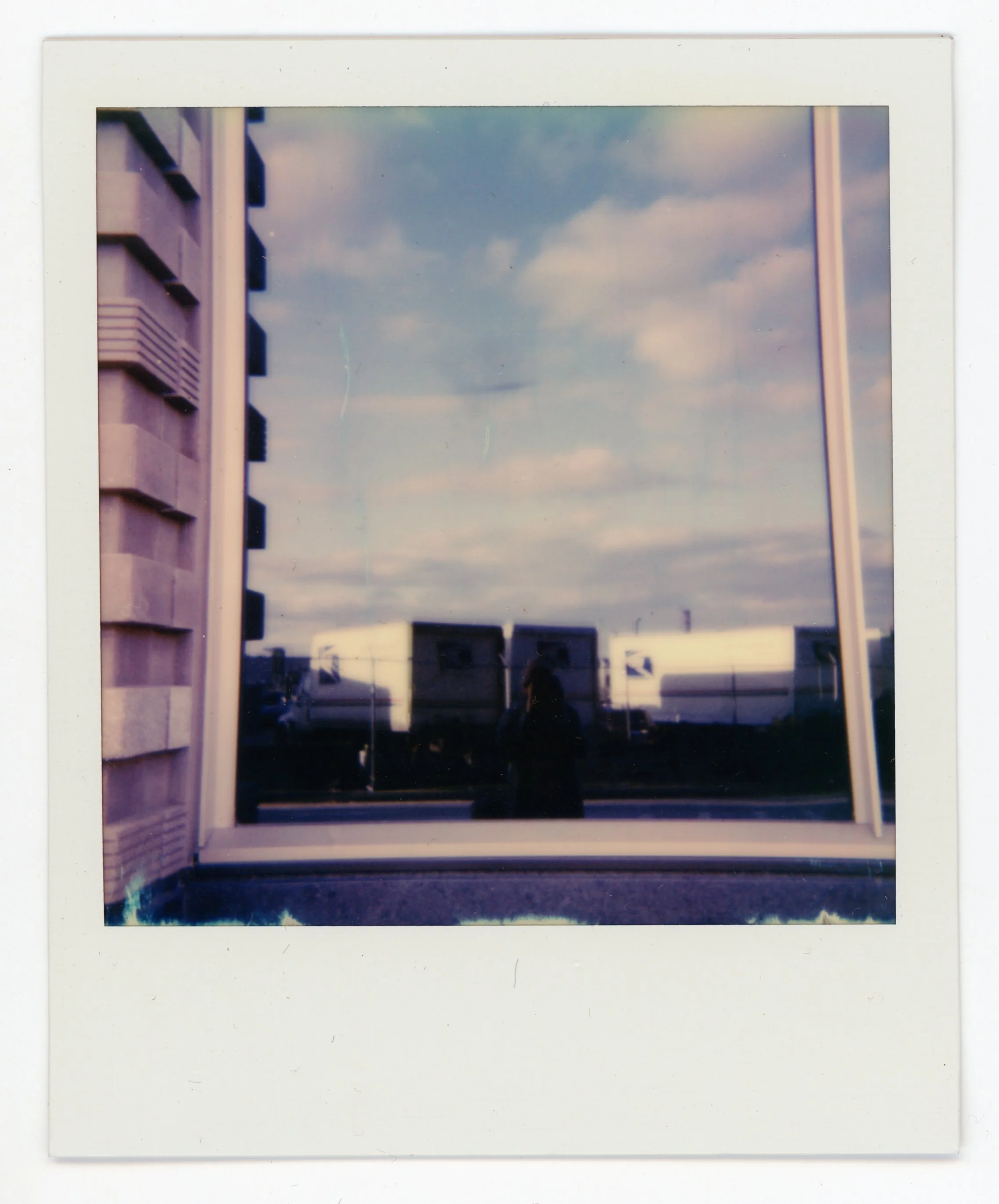 Reflection of a cloudy sky, a person, and a train in a window with a white frame